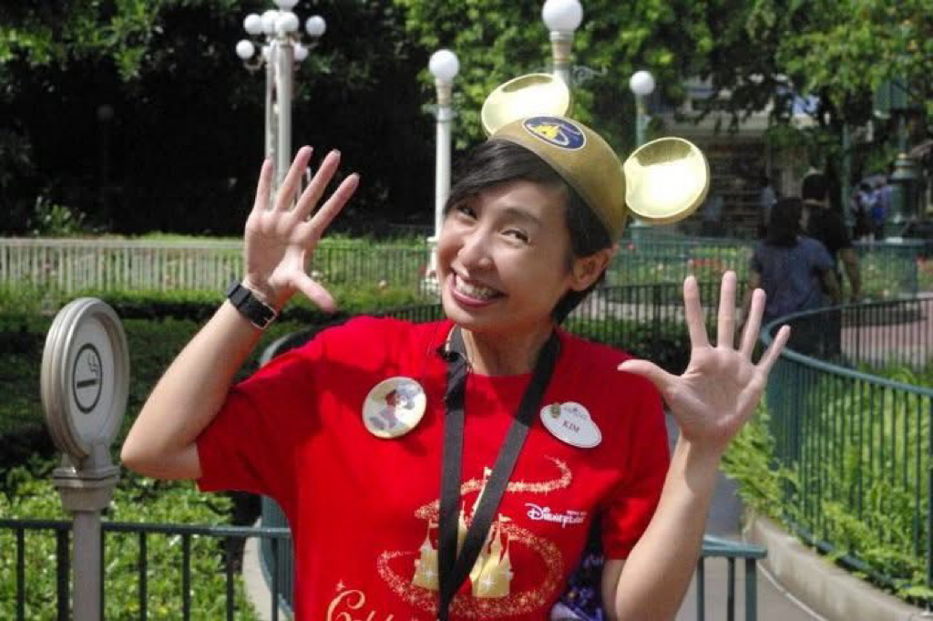 Kim smiling with her hands up and wearing gold Mickey ears.