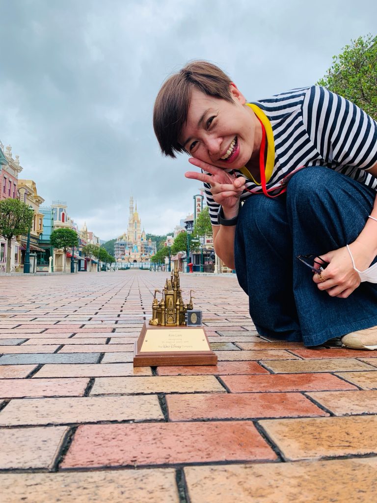 Kim holding up a peace sign with her Disney award at Hong Kong Disneyland.