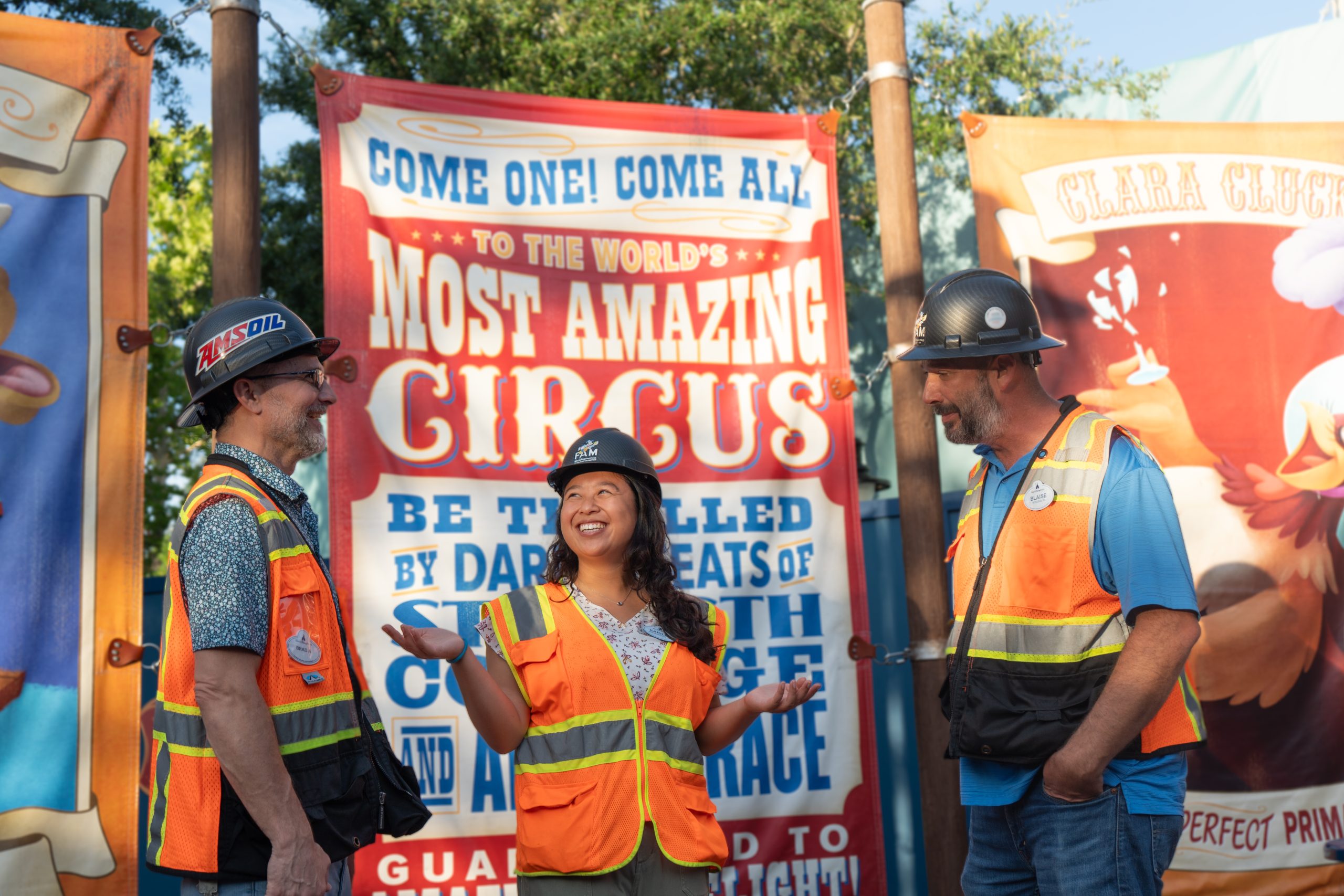 Karilin and coworkers smile in front of circus area in Walt Disney World in orange safety vests.