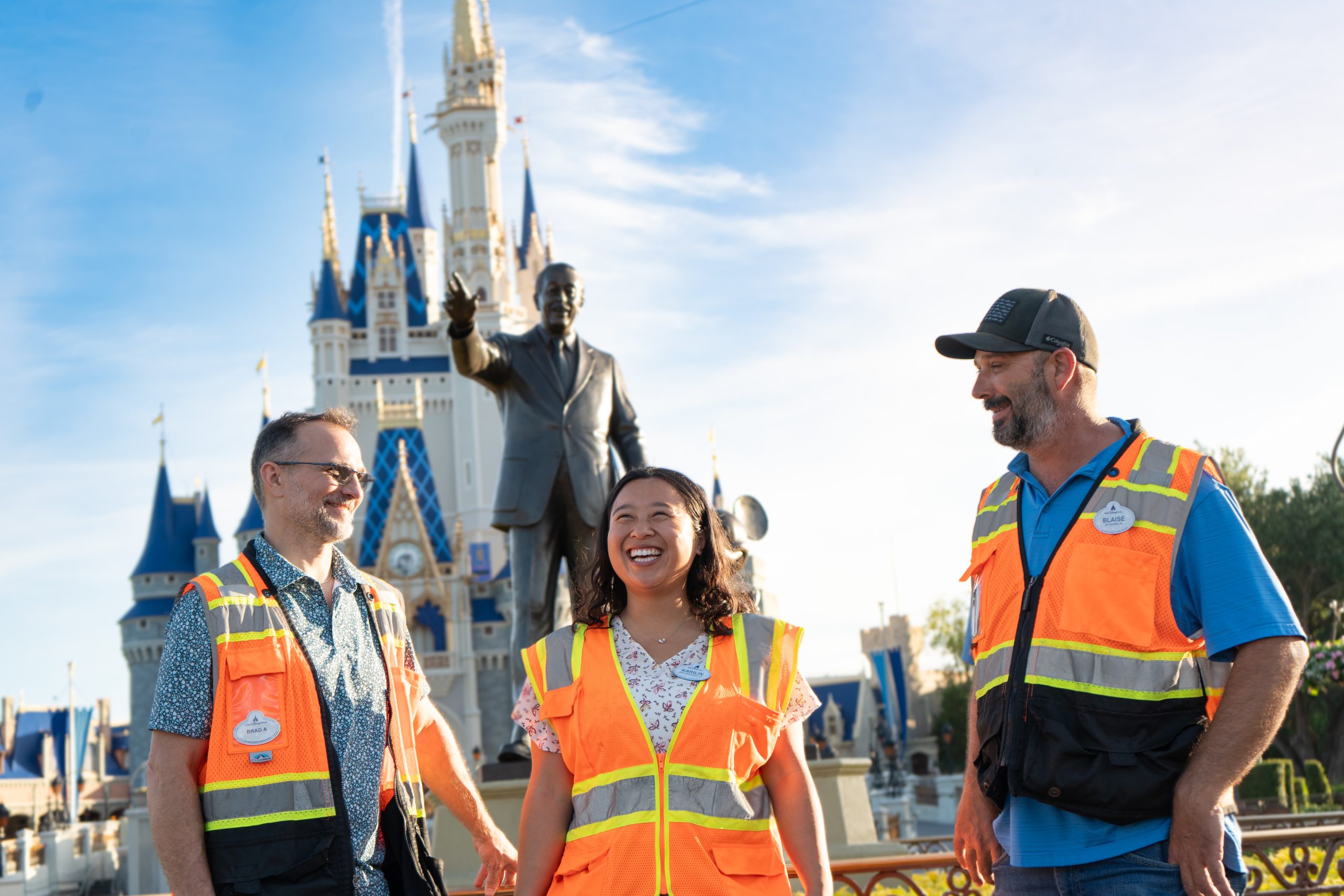 Karilin and coworkers smile in front of Cinderella's Castle in orange safety vests.