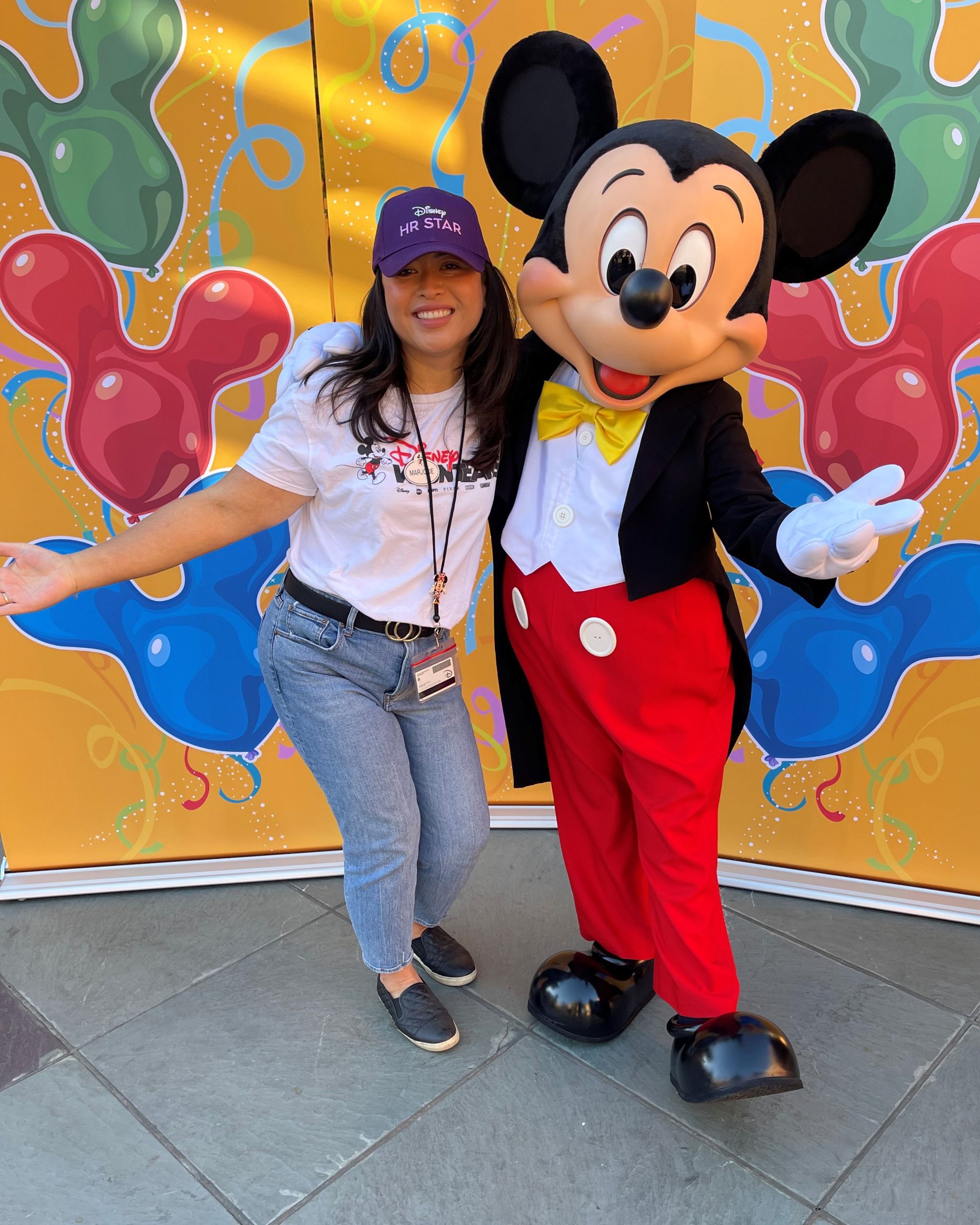 Disney recruiter Marjorie poses with Mickey Mouse during a Disney employee event, representing her journey from project hire to supporting candidate experience and talent acquisition.