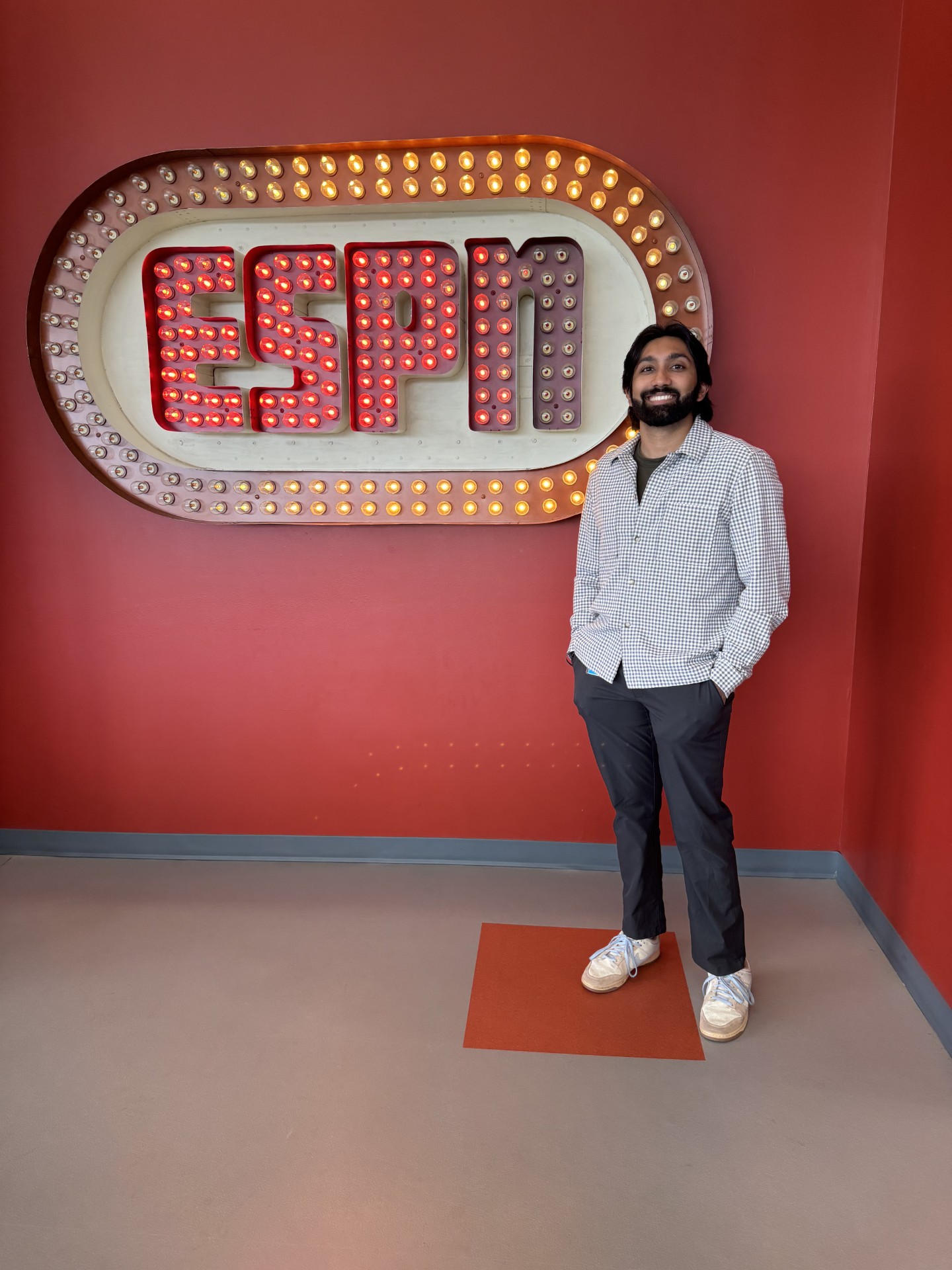 Person standing beside an illuminated ESPN sign with marquee-style lights on a red wall background.