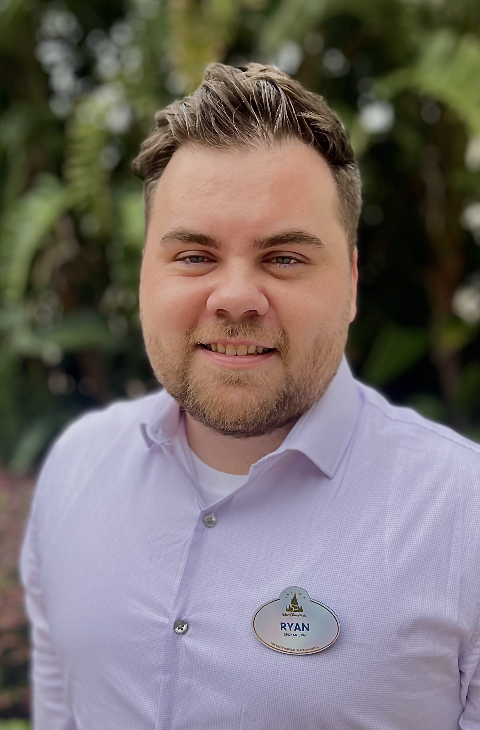 Smiling employee in a light purple shirt in front of a green background