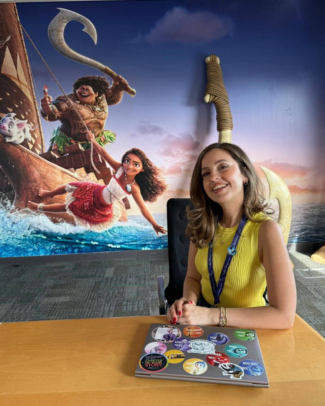 Disney recruiter Sevay sits in a Disney office space in front of a Moana-themed mural, representing the global career opportunities and storytelling culture that drew her to a recruiting career at Disney.