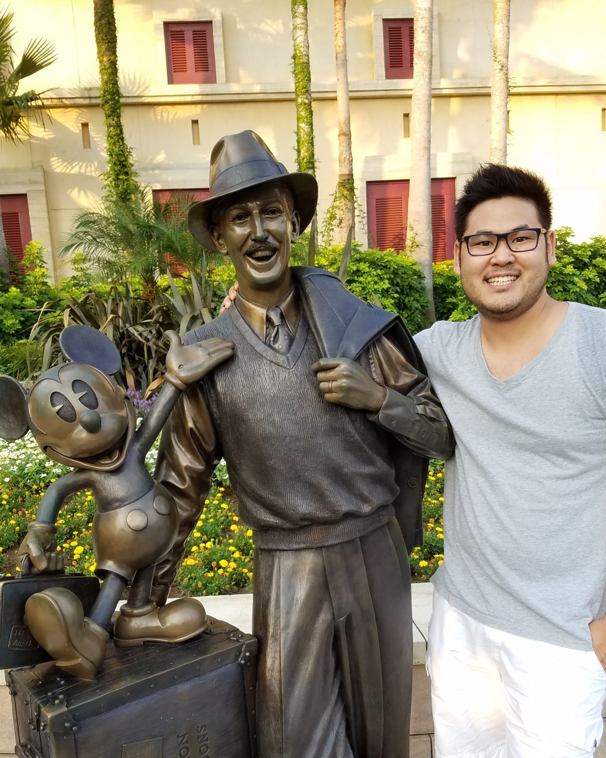 Disney recruiter Yoshi poses beside a statue featuring Walt Disney and Mickey Mouse, reflecting a career journey that started with the Disney College Program and grew into professional recruitment.