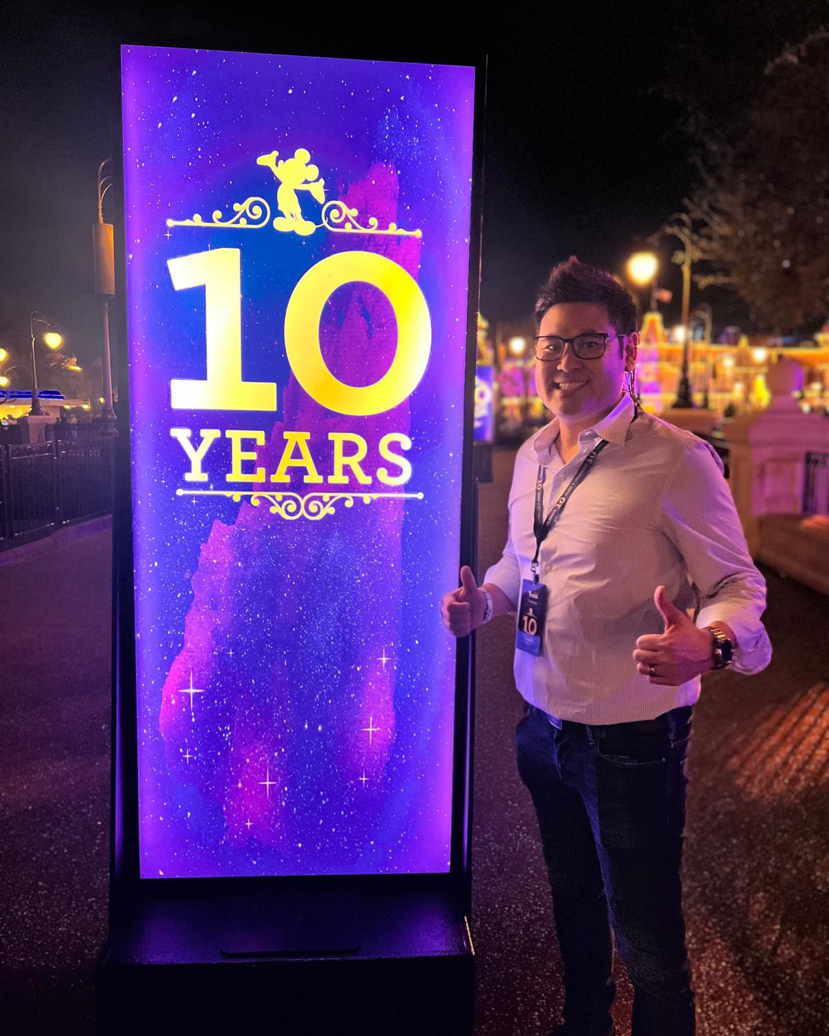 Disney recruiter Yoshi stands beside a Disney 10-year service celebration display, highlighting long-term career growth and advancement opportunities across The Walt Disney Company.