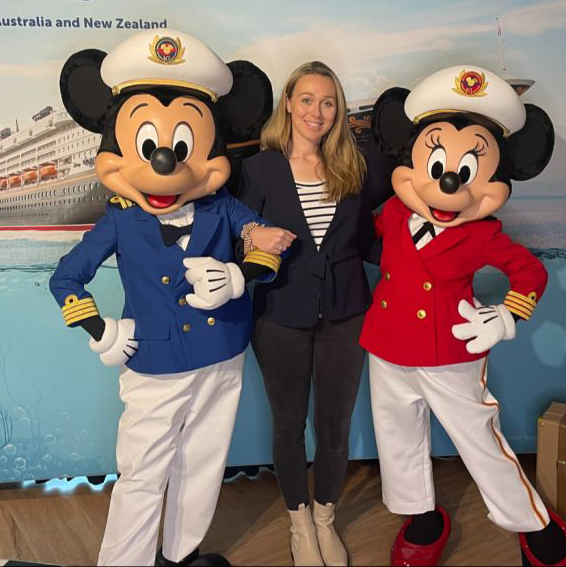 Smiling professional recruiter posing with Mickey and Minnie Mouse dressed as cruise ship captains in front of a Disney Cruise Line backdrop