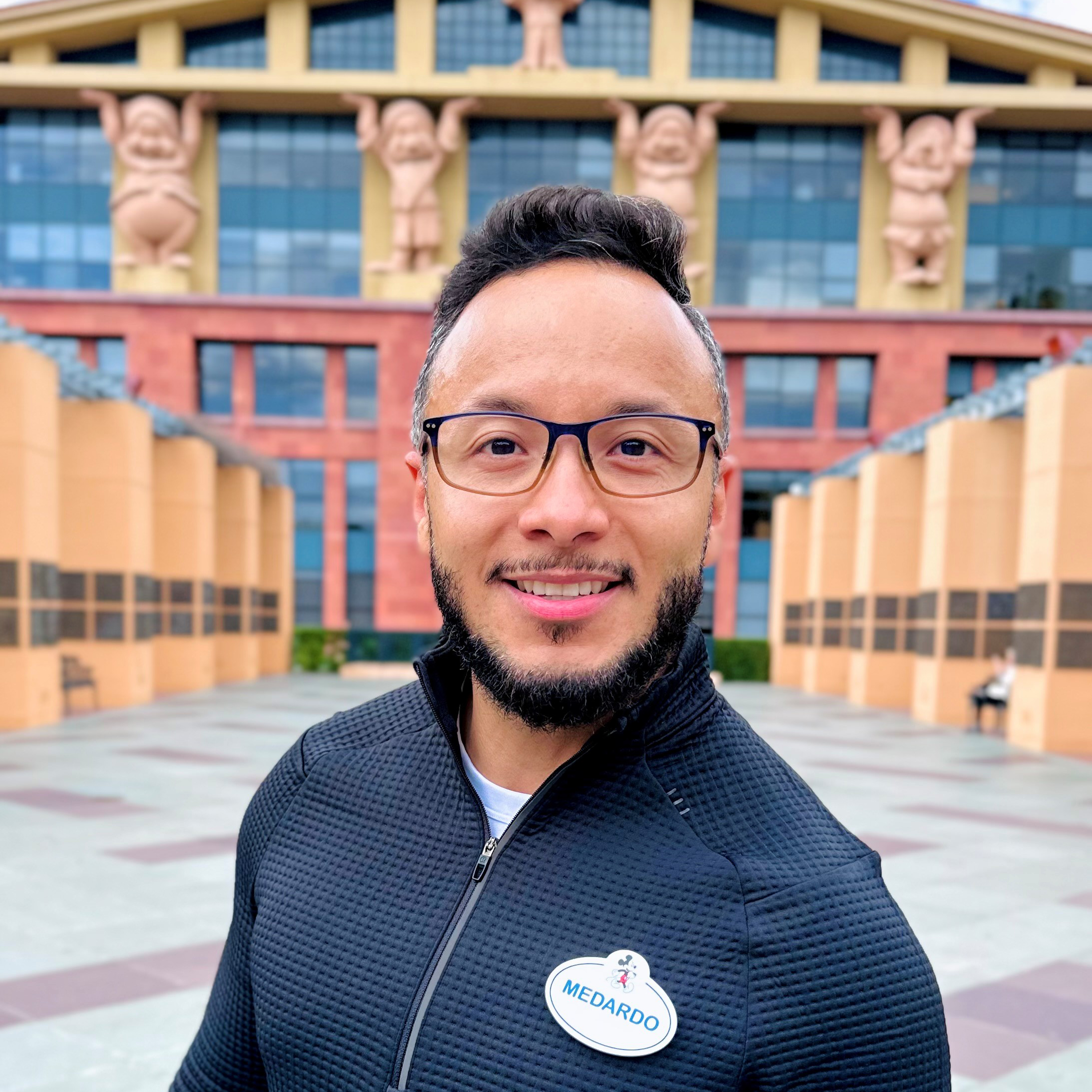 Smiling employee in a dark shirt in front of a Disney building.