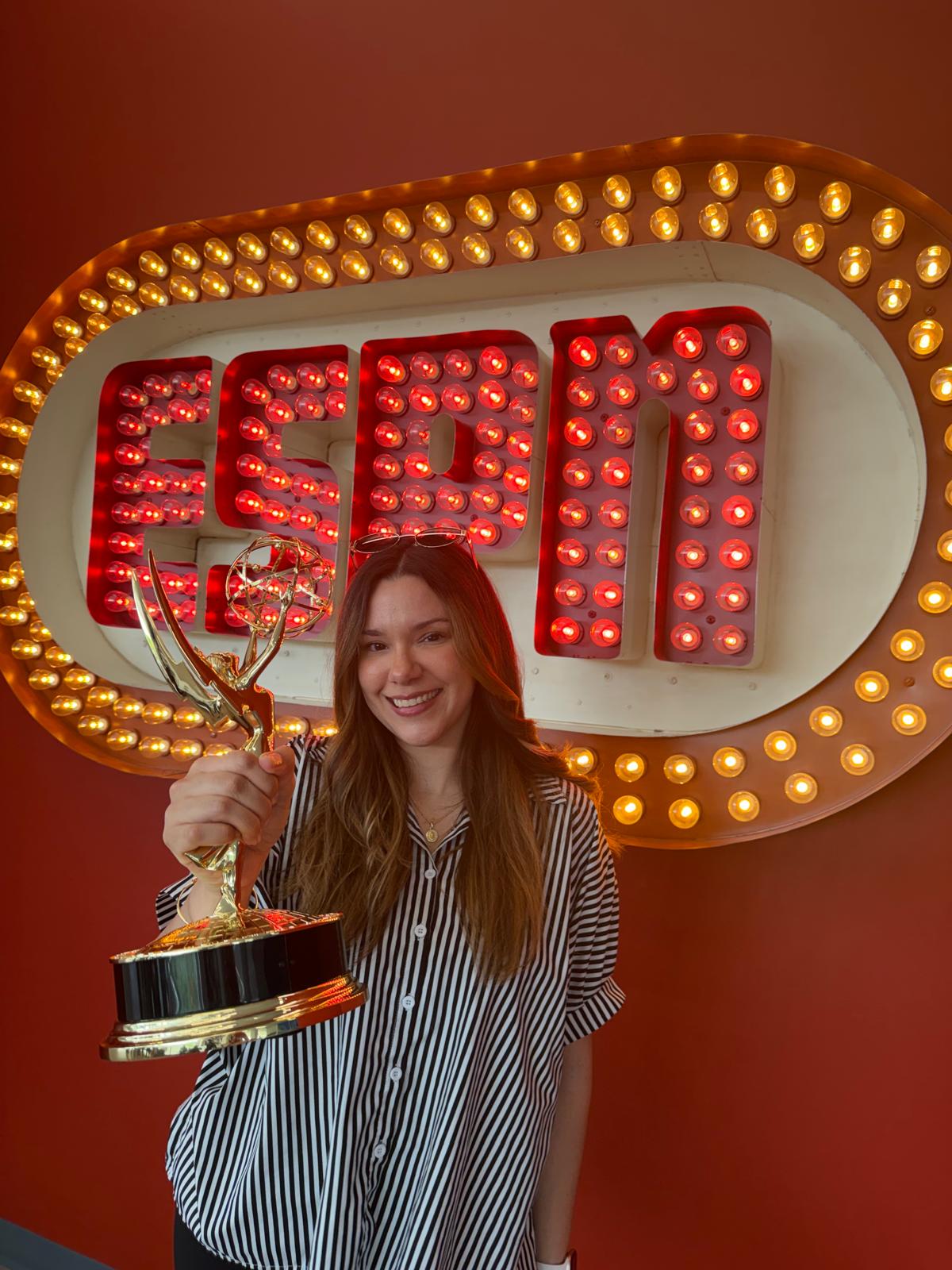 ESPN Associate Producer Mireya poses with an Emmy Award in front of an ESPN sign, highlighting career growth and achievement in sports broadcasting and live television production.