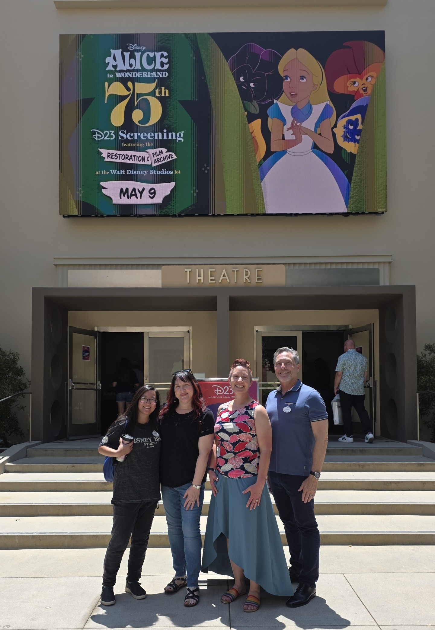 Disney film restoration team outside a theater marquee reading &ldquo;Alice in Wonderland 75, D23 Screening, Restoration Celebration, May 9.&rdquo;