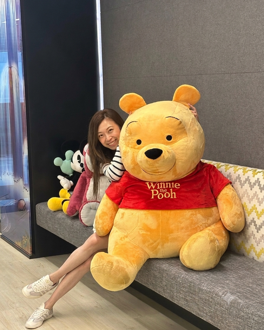 APAC Cast Member smiling while sitting behind a large Winnie the Pooh plush stuffed animal