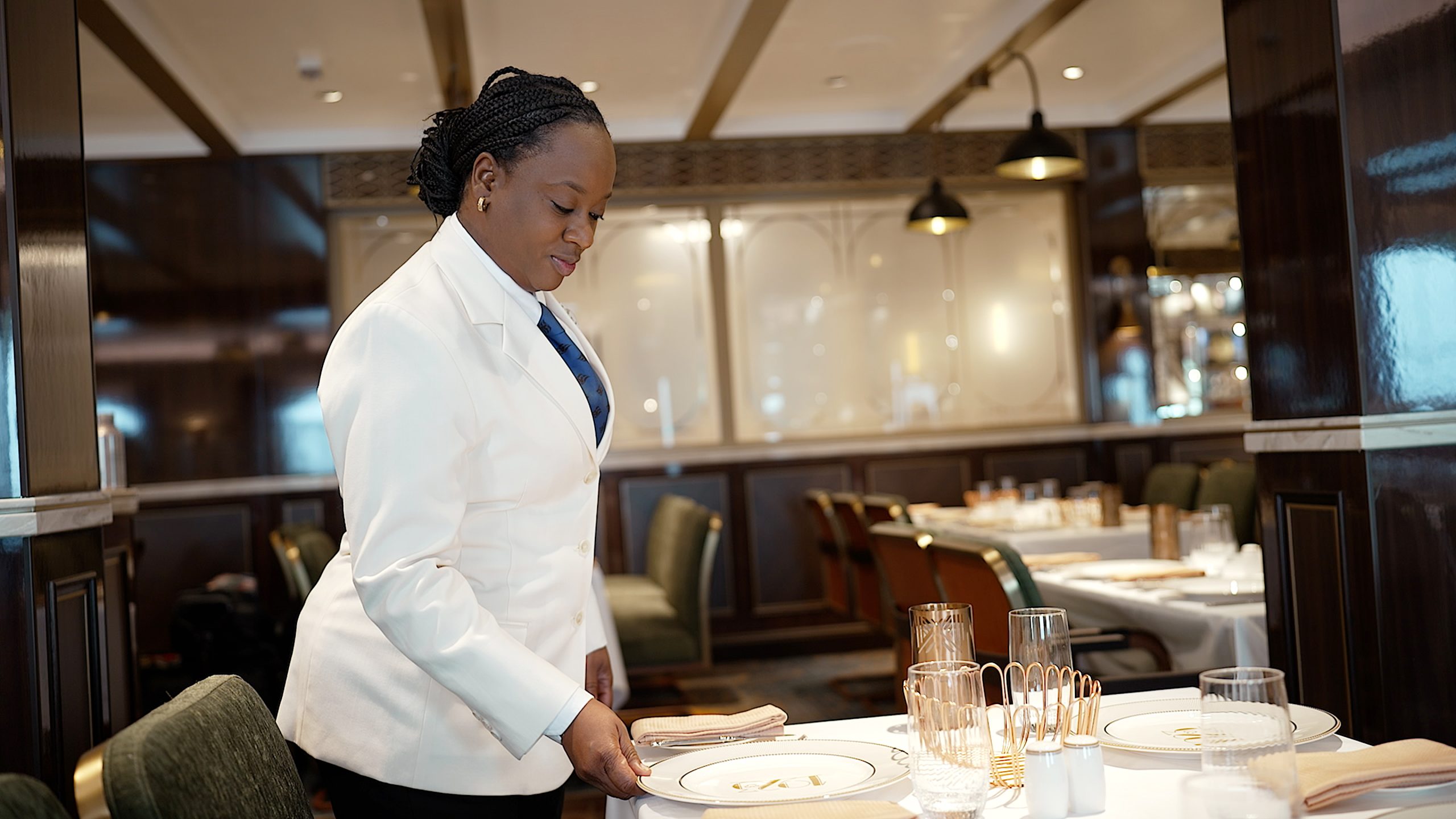 Cindy, Restaurant Manager aboard the Disney Treasure, sets a dining table as part of her work supporting safe restaurant operations aboard the Disney Cruise Line ship