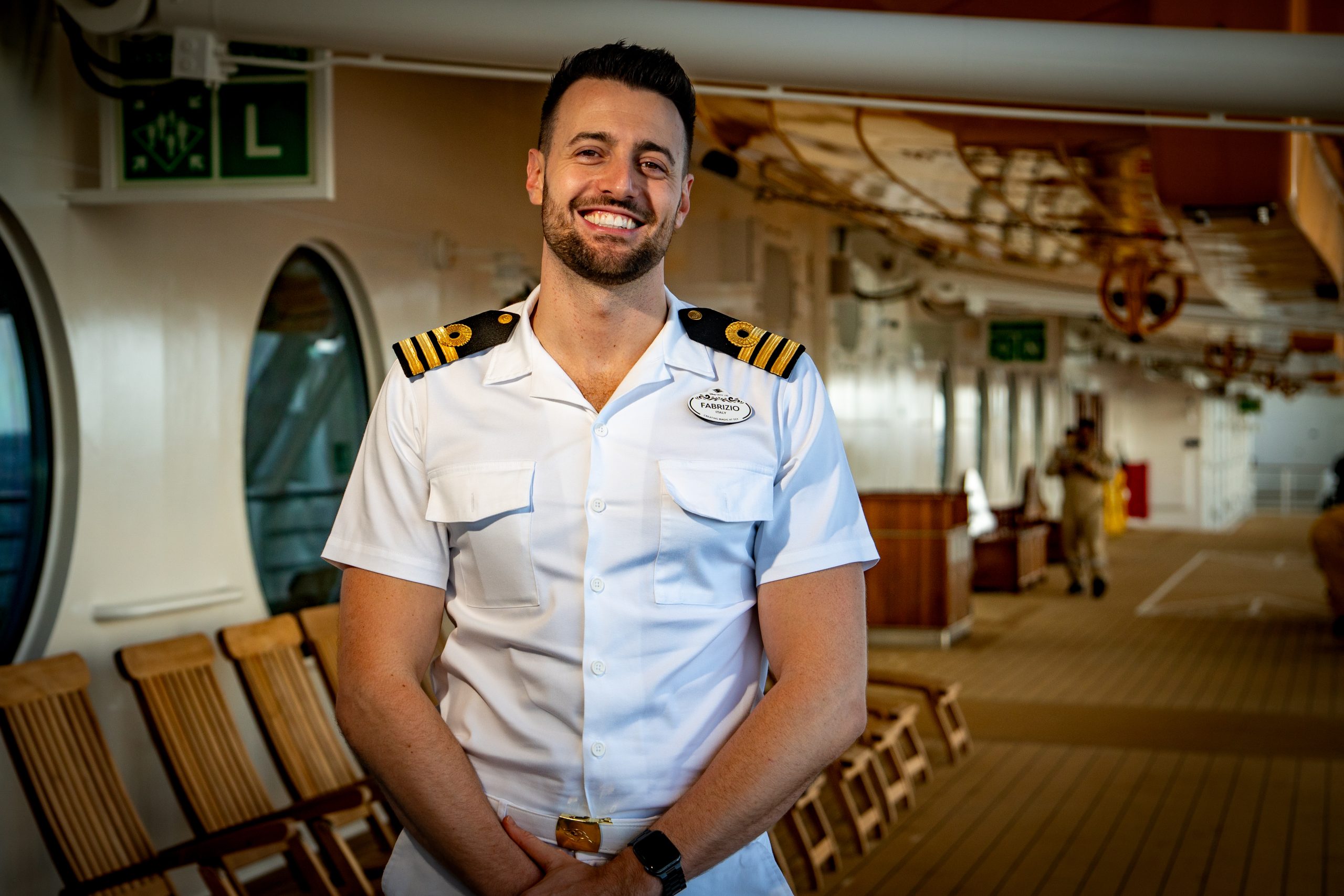 Fabrizio, Chief Officer aboard the Disney Destiny, stands on an outdoor ship deck in his white officer uniform while discussing the importance of Disney Cruise Line safety training.