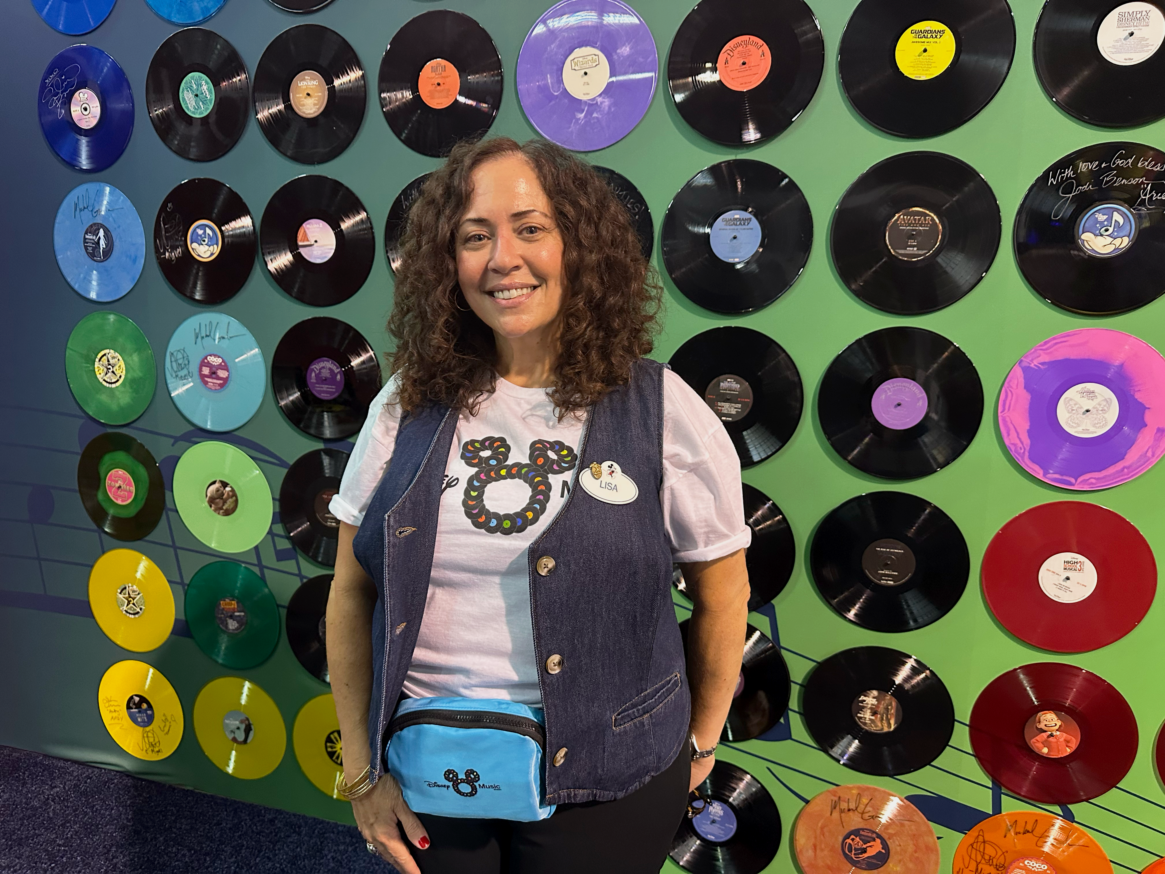 A Disney Music Group team member stands in front of a display of Disney soundtrack vinyl records at D23: The Ultimate Disney Fan Event, celebrating the music, creativity, and entertainment careers that help bring Disney stories to life through sound.