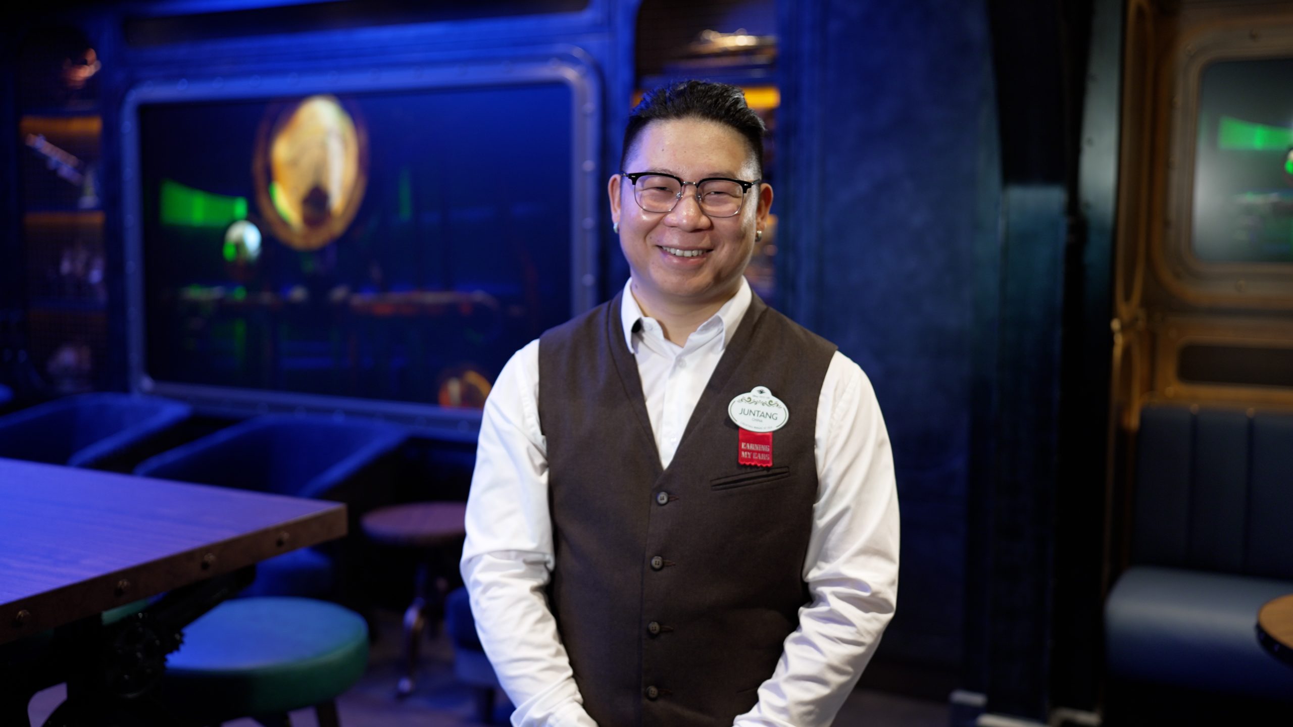 Jungtang, a bartender aboard the Disney Adventure, stands inside a shipboard venue while sharing the importance of safety training for Disney Cruise Line crew members.