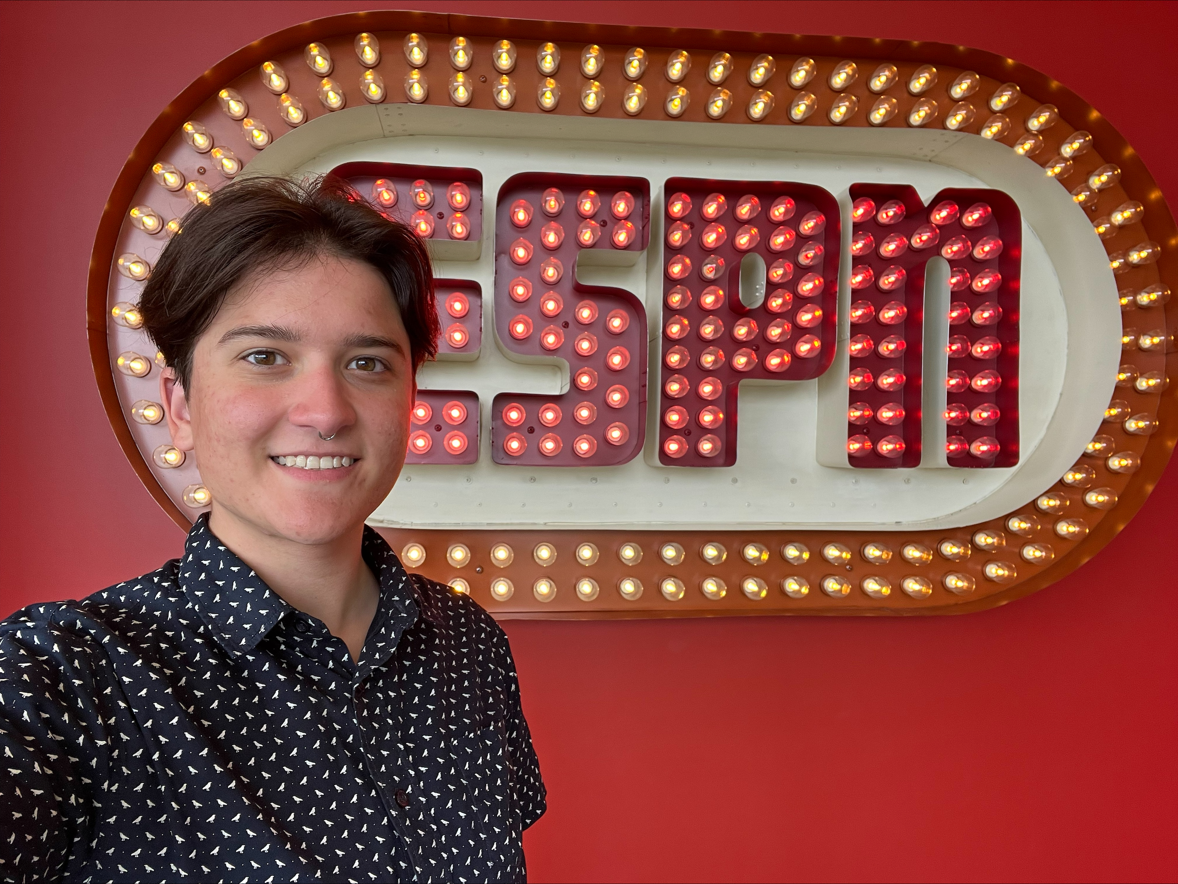 Mac, an ESPN Content Associate and NLGJA member, smiles beside an illuminated ESPN logo.