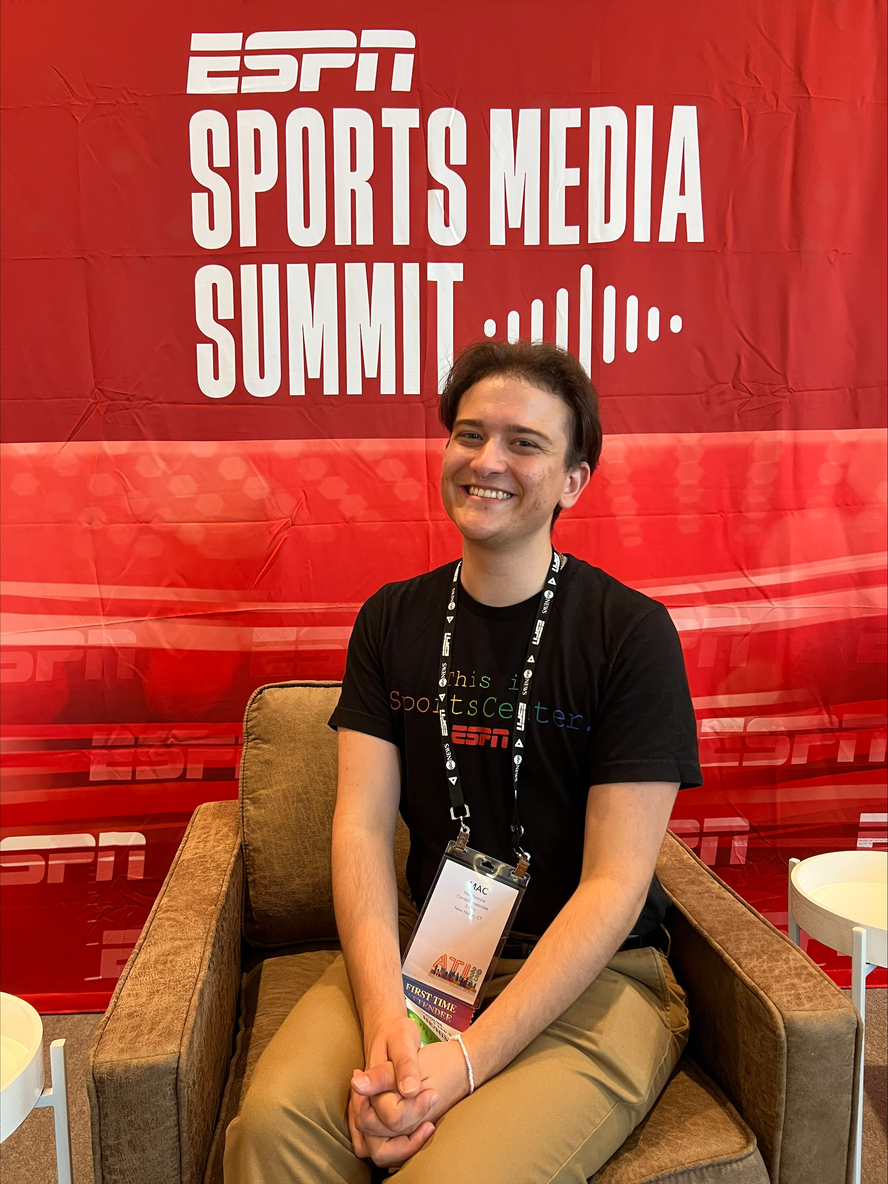 Mac, an ESPN Content Associate, sits in front of a red &ldquo;ESPN Sports Media Summit&rdquo; backdrop while wearing an event credential.