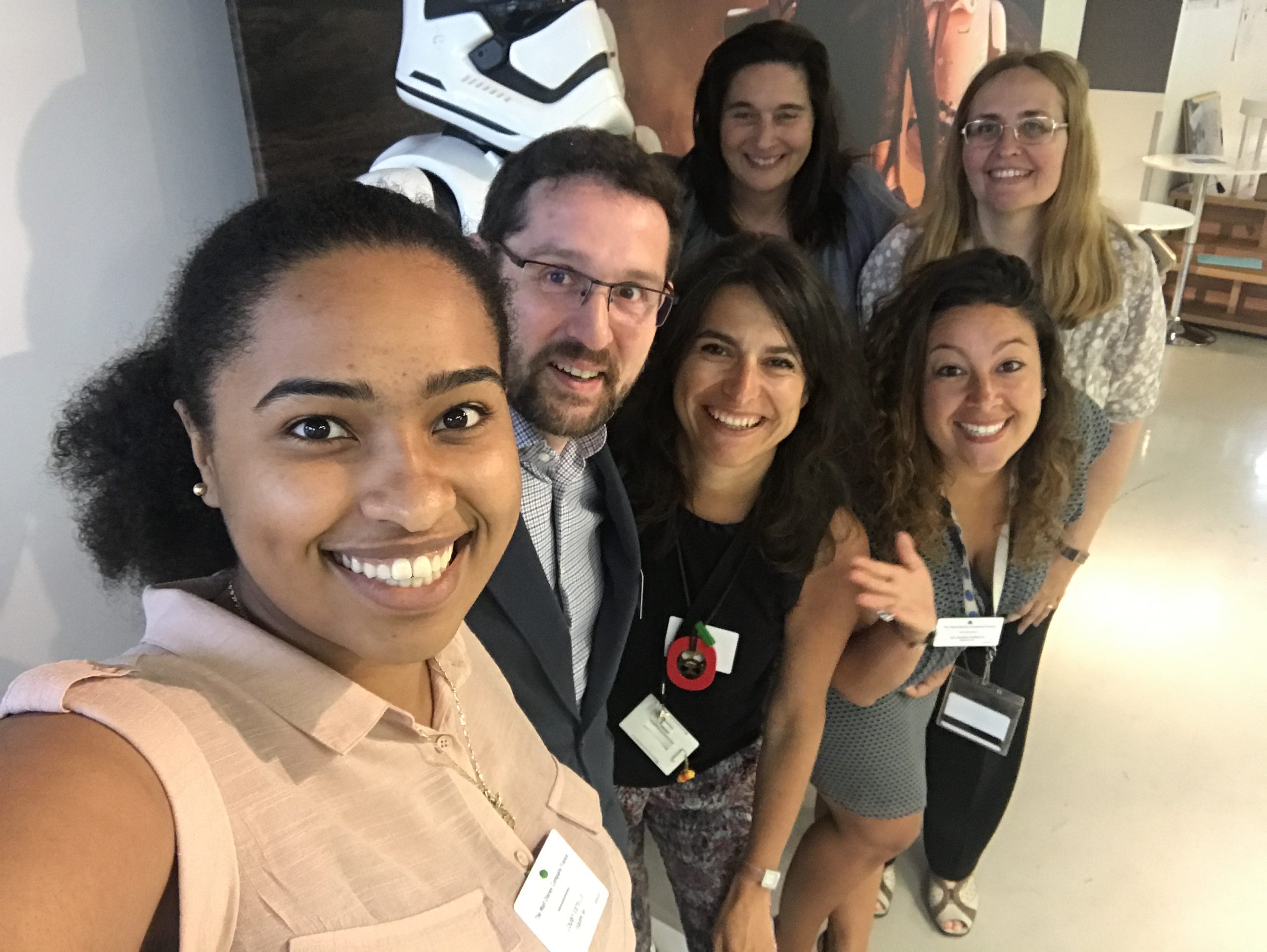 A group of colleagues gathers closely and smiles for a selfie in an office setting