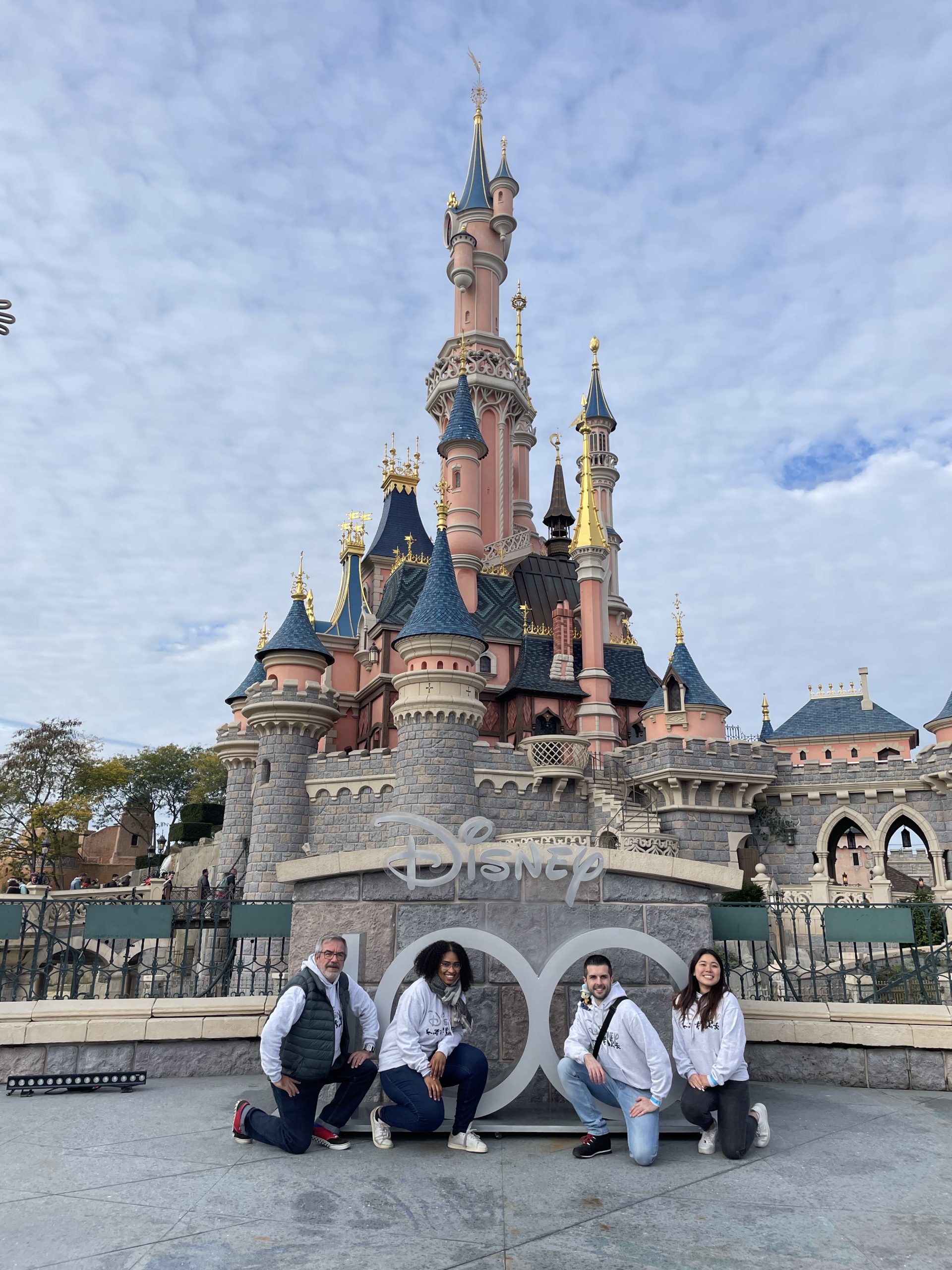 Four people pose near a Disney100 display with the Disneyland Paris castle in the background.