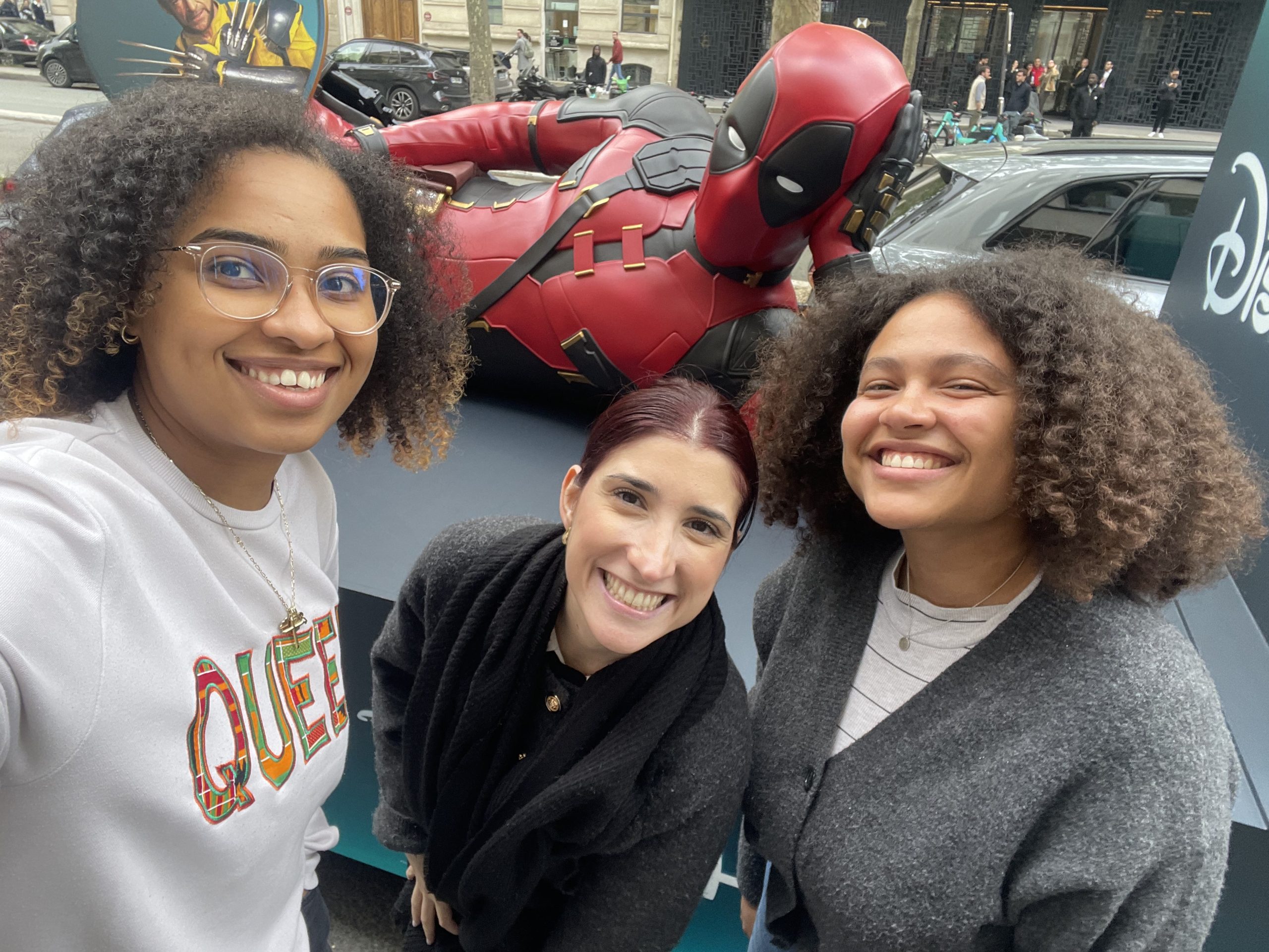 Three people smile for a photo in front of a Deadpool display.