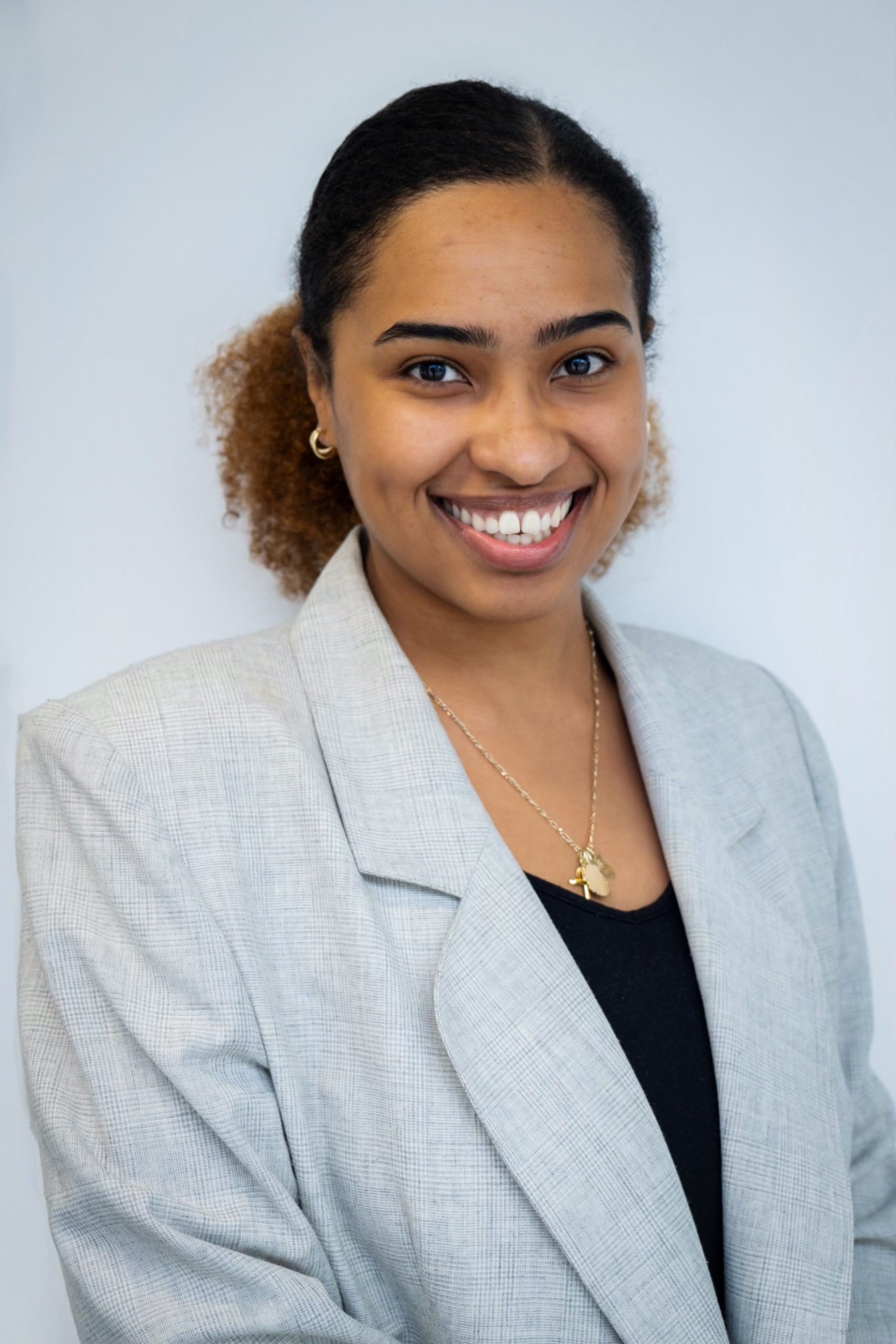 Professional headshot of a smiling employee wearing a light gray blazer against a pale background.