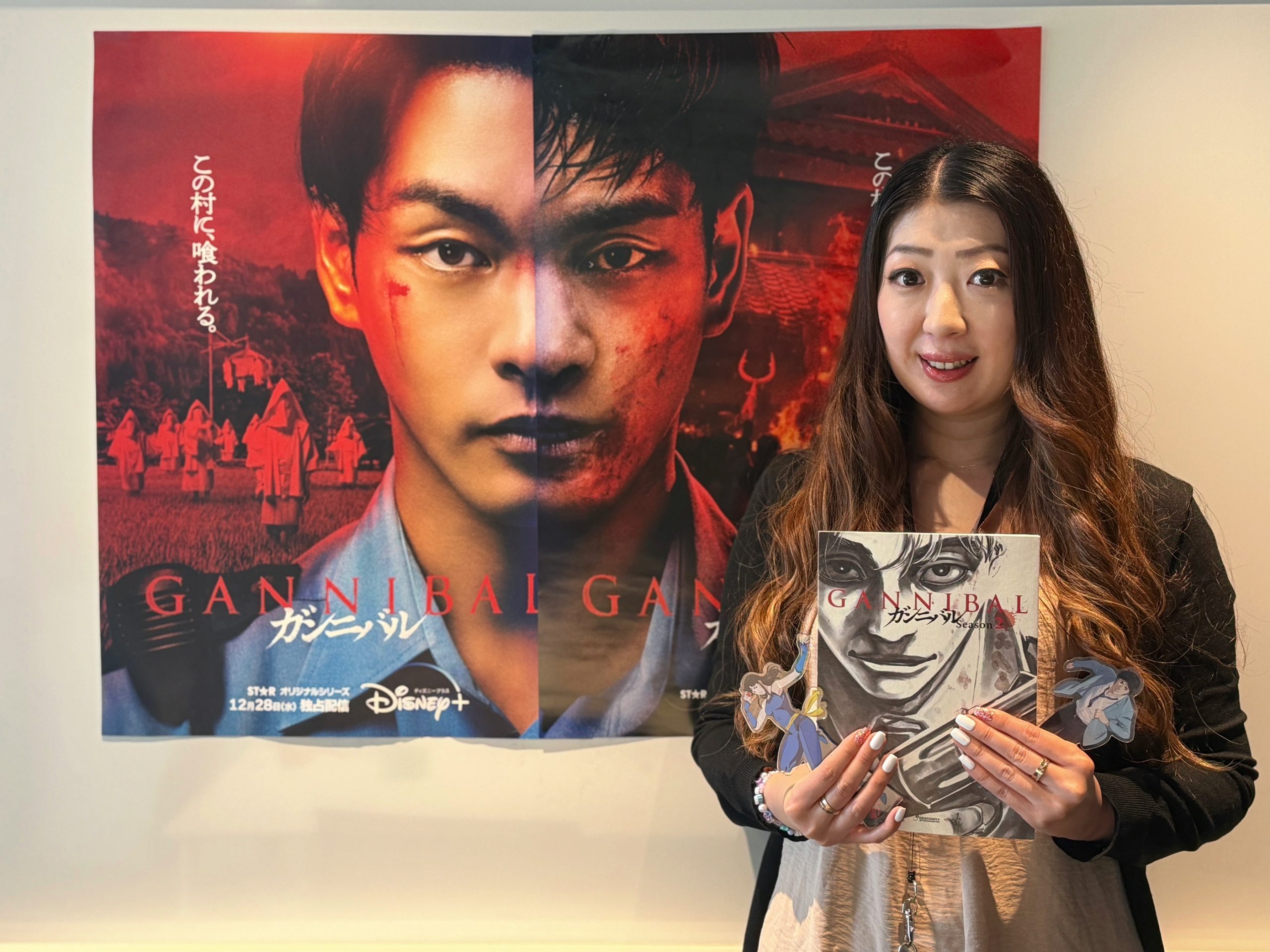 Yumi from Disney Japan holds Gannibal artwork in front of a display promoting the Japanese Disney+ series.