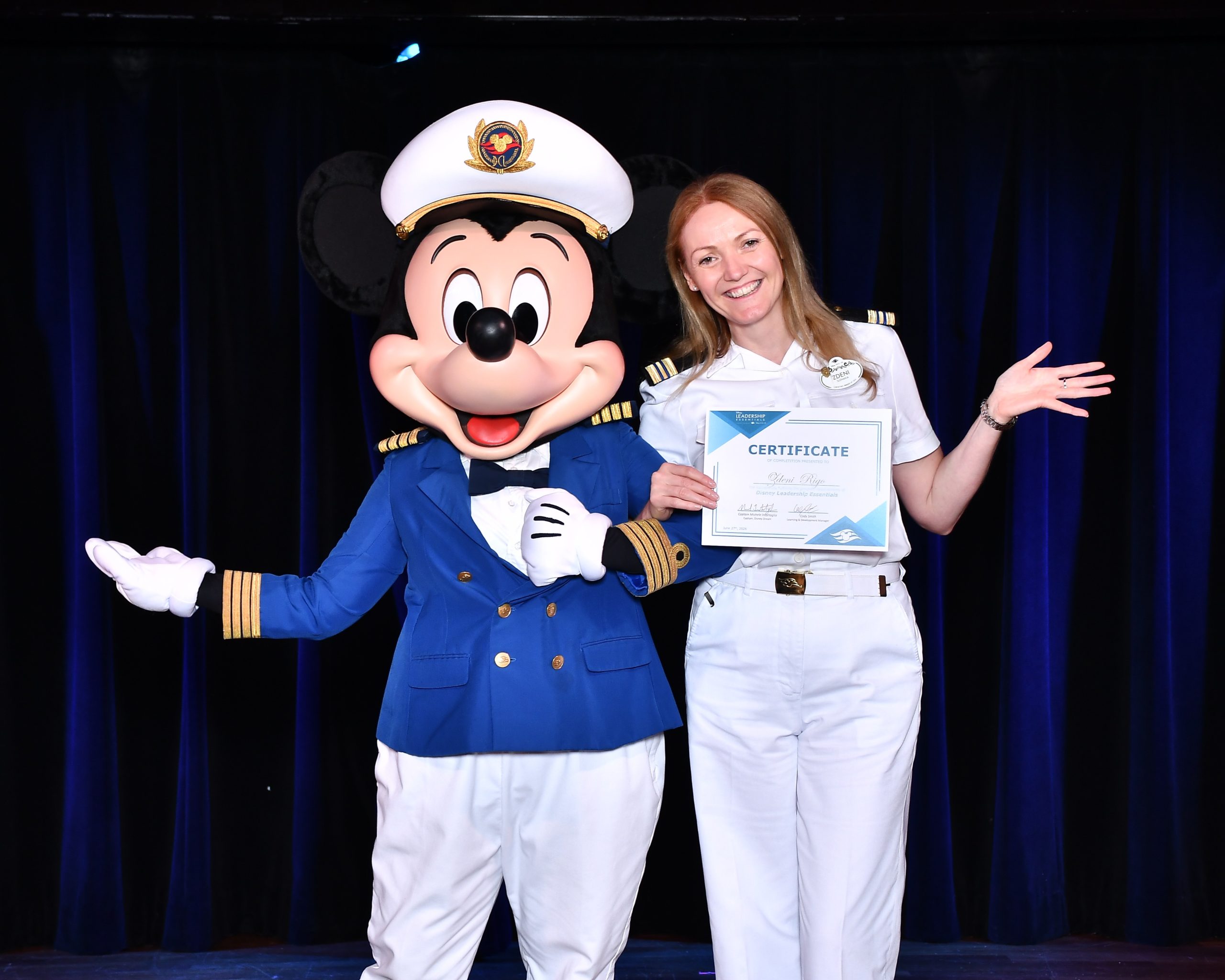 Disney Cruise Line Human Resources Manager Zdeni holds a recognition certificate while posing with Mickey Mouse onboard.