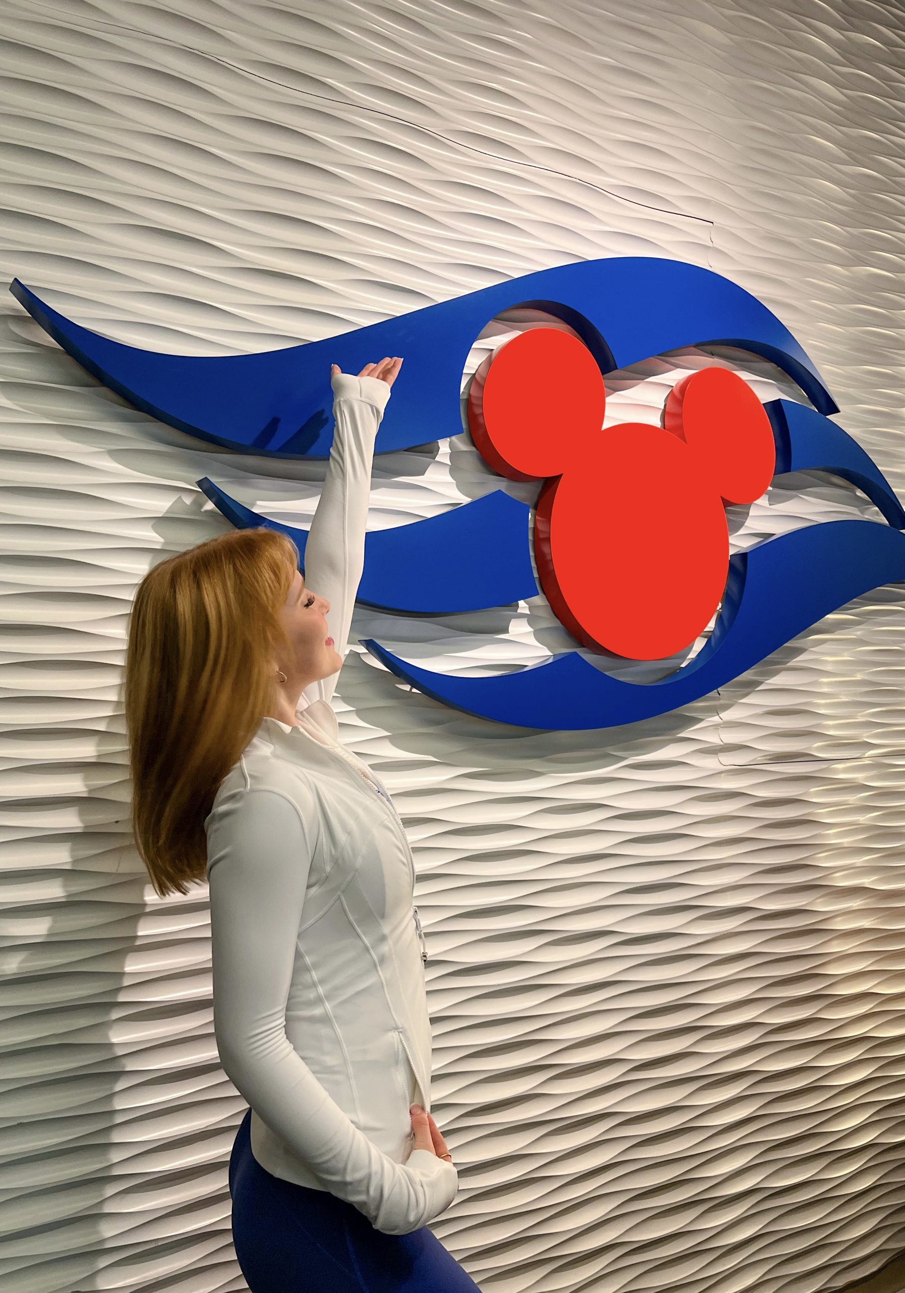 Image of Caroline, Performer smiling and looking back at white wall with Disney Cruise Line logo
