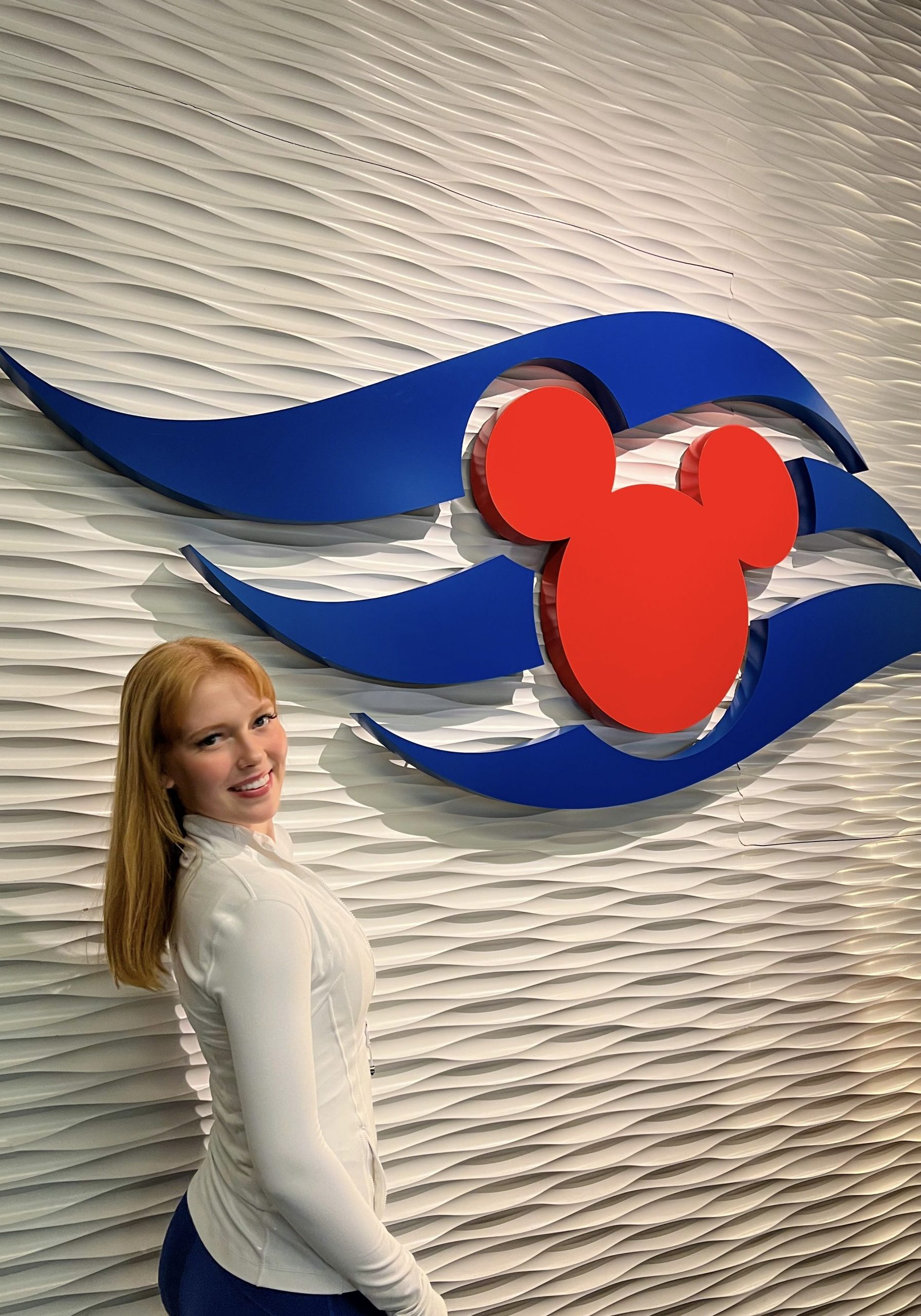 Image of Caroline, Performer smiling in front of white wall and Disney Cruise Line logo