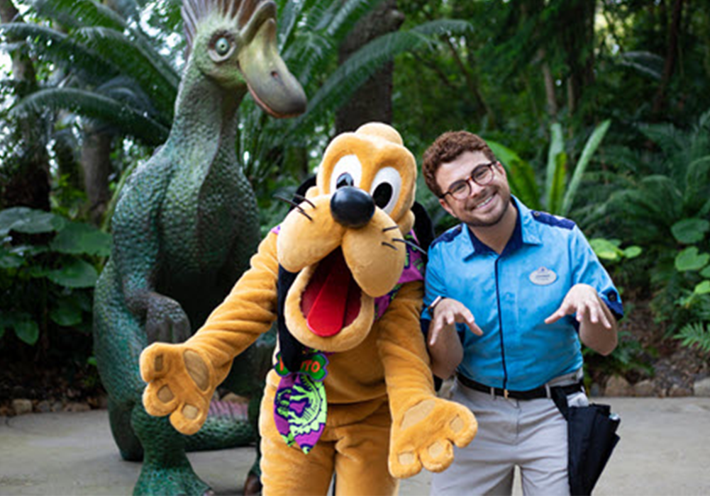 Disney college program entertainment male cast member smiling and standing with his hands imitating animal paws while standing next to Pluto at the Walt Disney World Resort