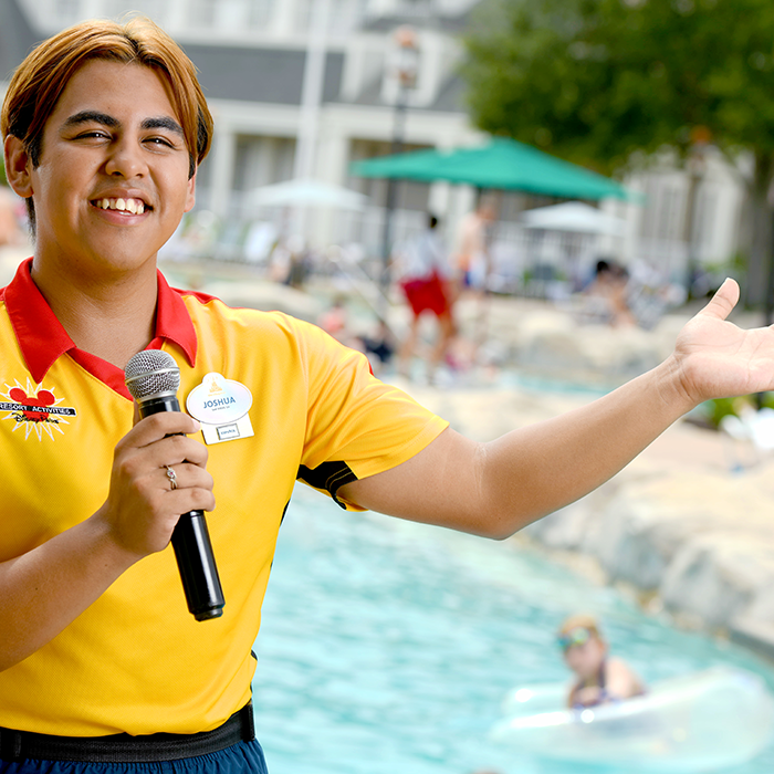Disney college program cast member holding a microphone and smiling in front of a pool at a Walt Disney World Resort