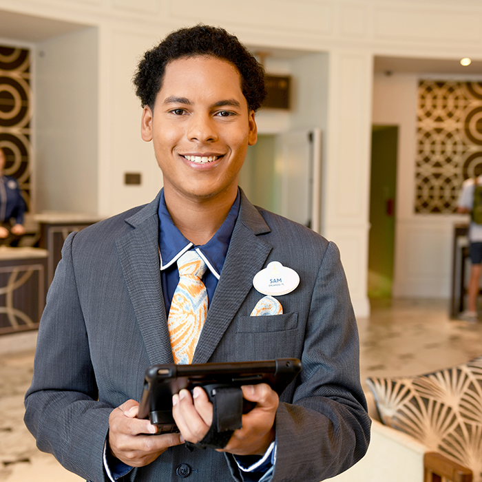 Disney college program lodging male cast member smiling while holding an Ipad in the lobby of a Walt Disney World Resort hotel