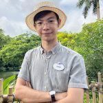 Image of employee with arms crossed in front of green foliage background