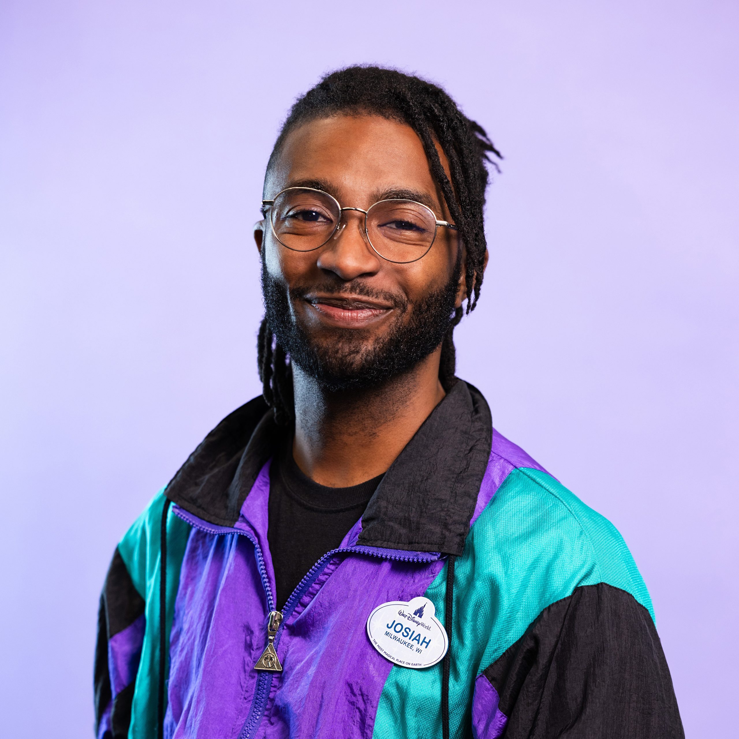 Life at Disney Podcast Season 3 host, Josiah with black hair, glasses and a colorful collared jacket