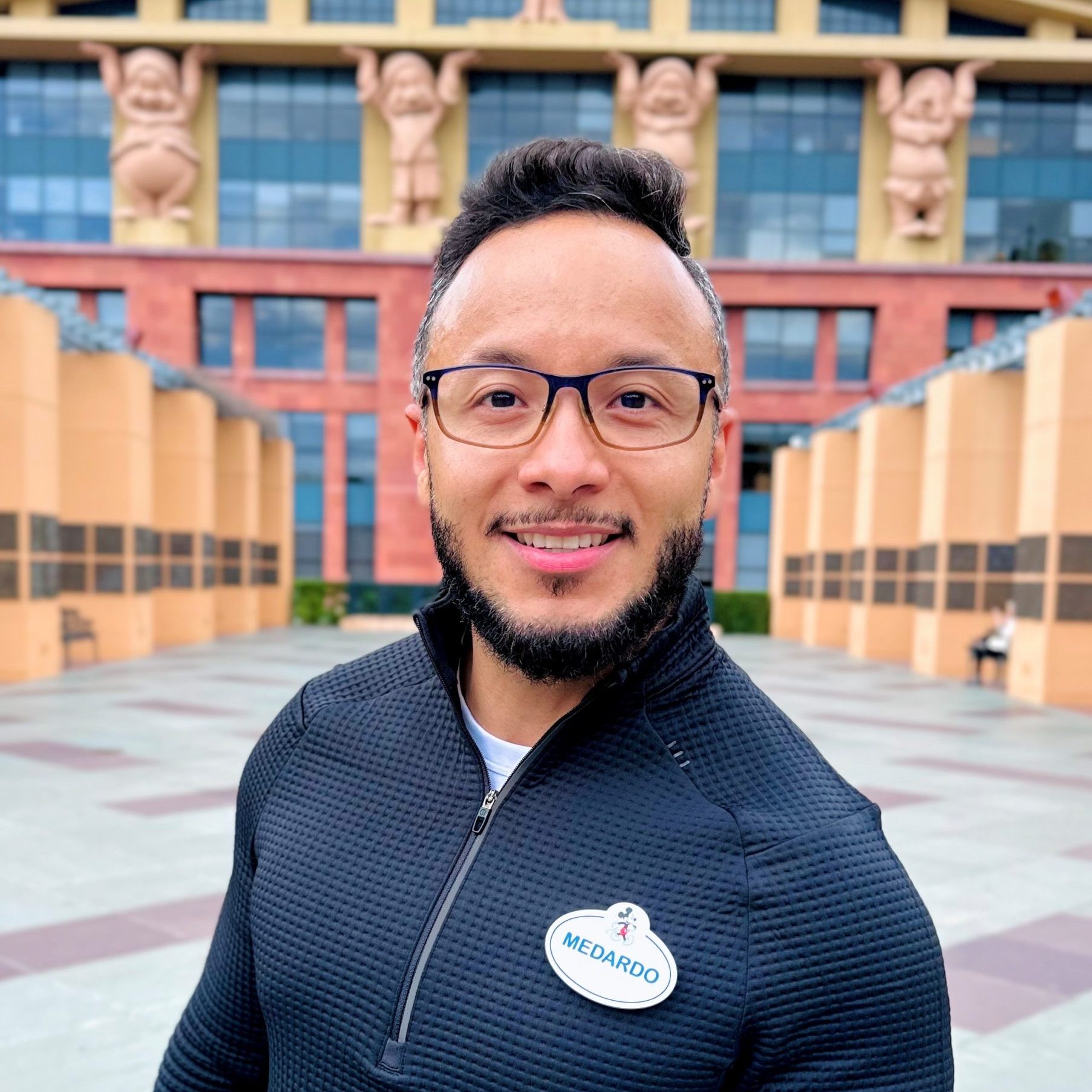 Photo of employee in a dark shirt in front of a Disney building.
