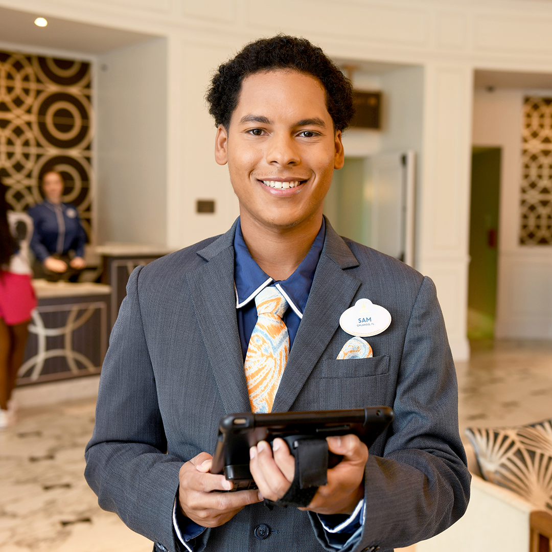 Disney college program lodging male cast member smiling while holding an Ipad in the lobby of a Walt Disney World Resort hotel