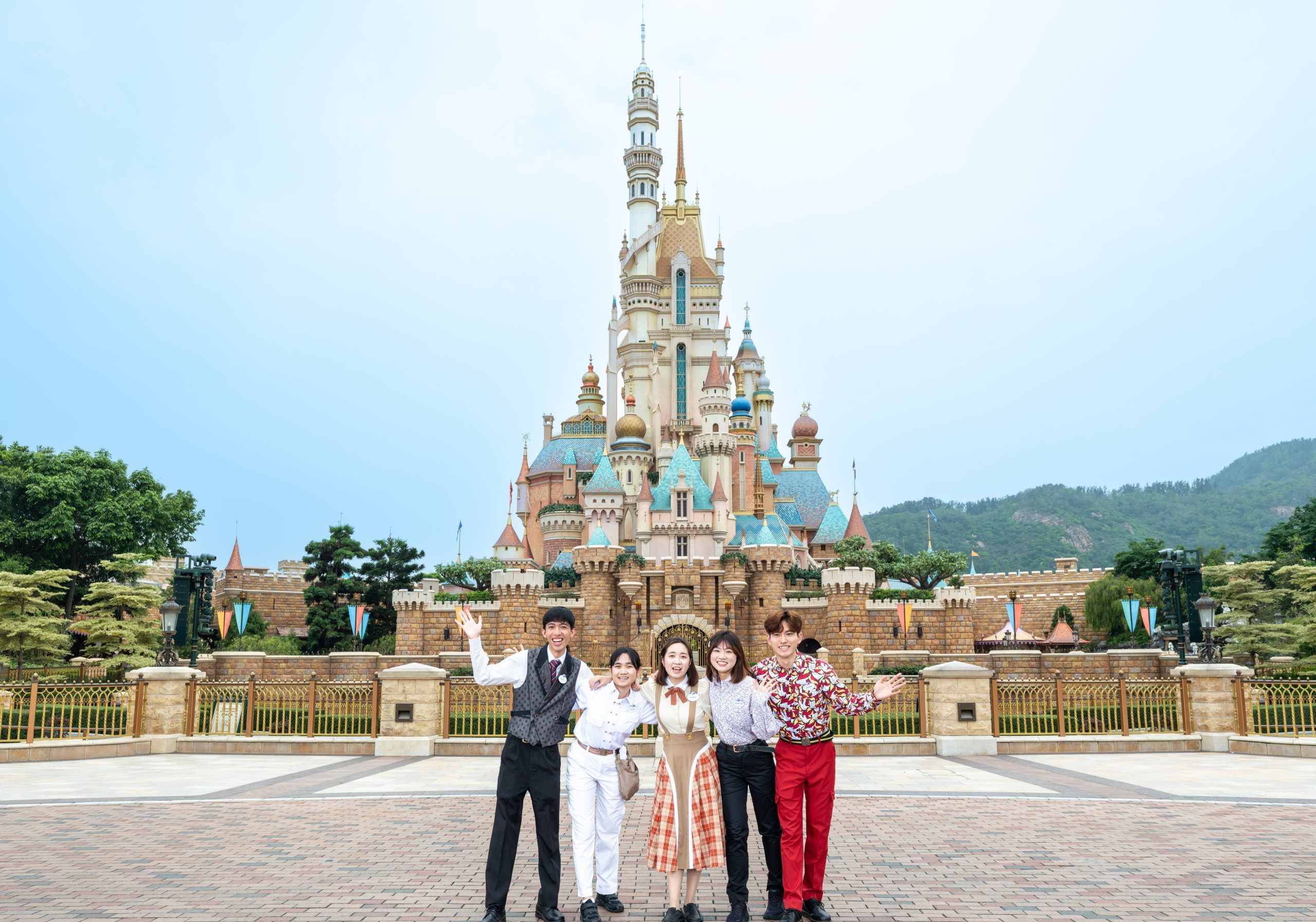 Image of five employees waving in front of castle at Hong Kong Disneyland