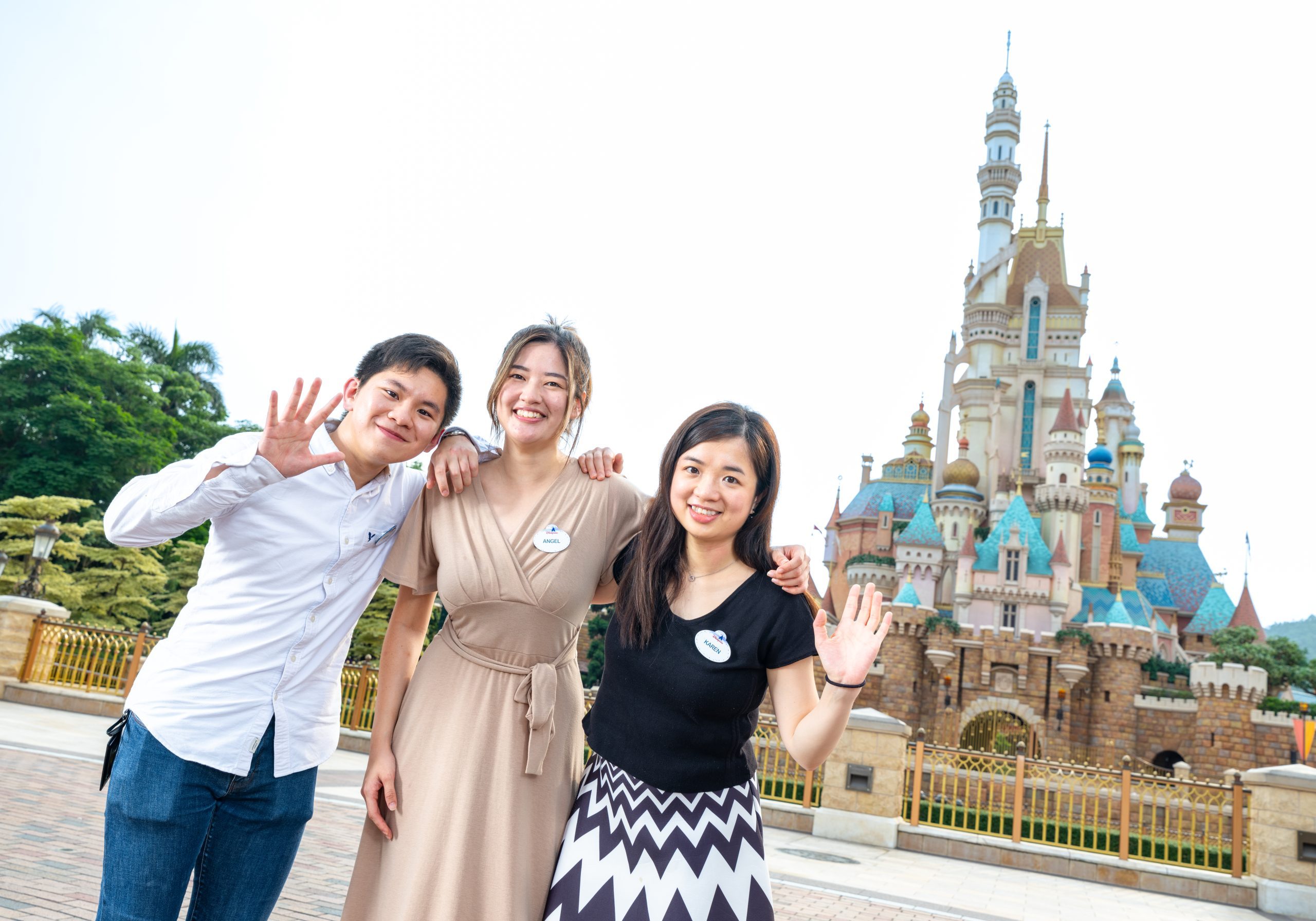 Image of three employees waving to the camera in front of castle at Hong Kong Disneyland