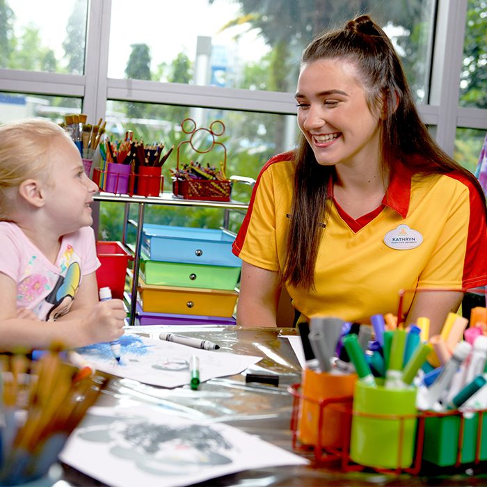Disney college program female cast member for children's services sitting at an arts and crafts table with a child smiling