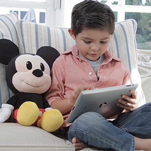 Little Boy reading on a couch with a Mickey Mouse plushie