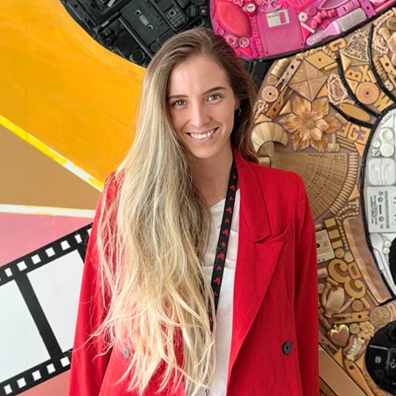 Estágios na Disney América Latina Recrutadora Emiliana sorrindo com longos cabelos loiros enquanto usava um casaco vermelho.