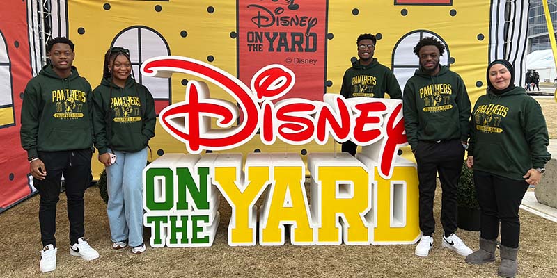 Five Disney on the Yard Innovation Challenge participants wearing Hampton University Pirates sweaters smiling with the Disney on the Yard logo at a competition event