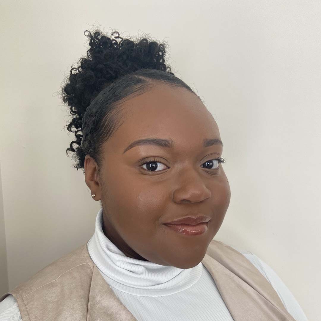 Howard University and Rhoden Fellow participant Takier smiling. She is wearing a white turtle neck and beige vest, and her hair is up in a bun