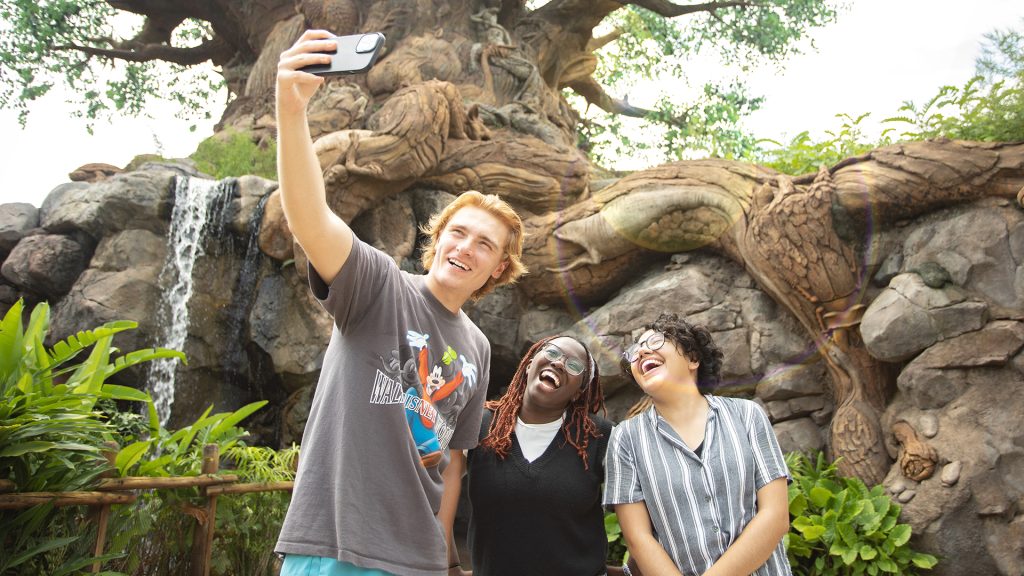 Three smiling young adults taking a selfie in front of the Tree of Life at Disney's Animal Kingdom