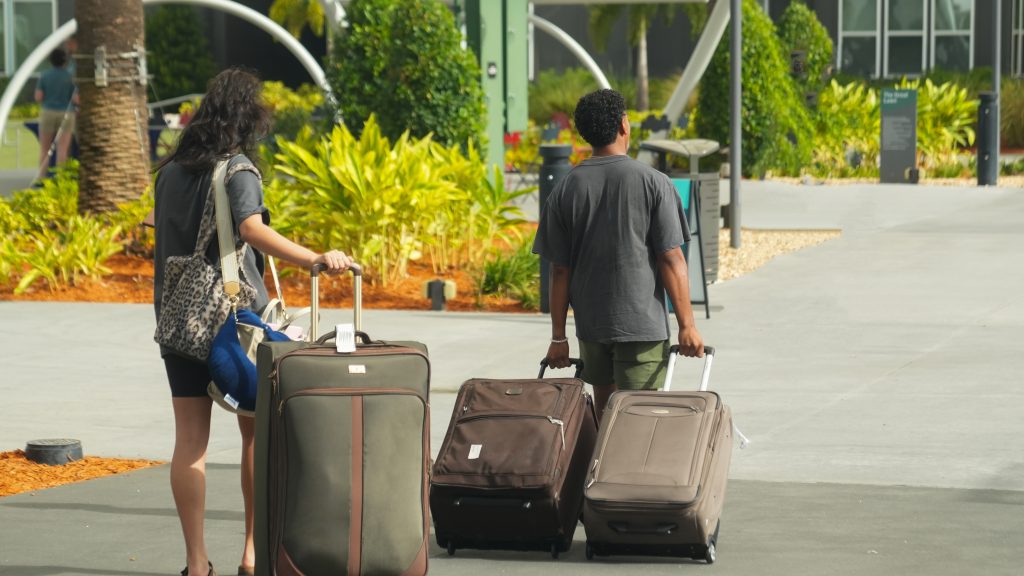 Two people walking away from the camera and carrying suitcases