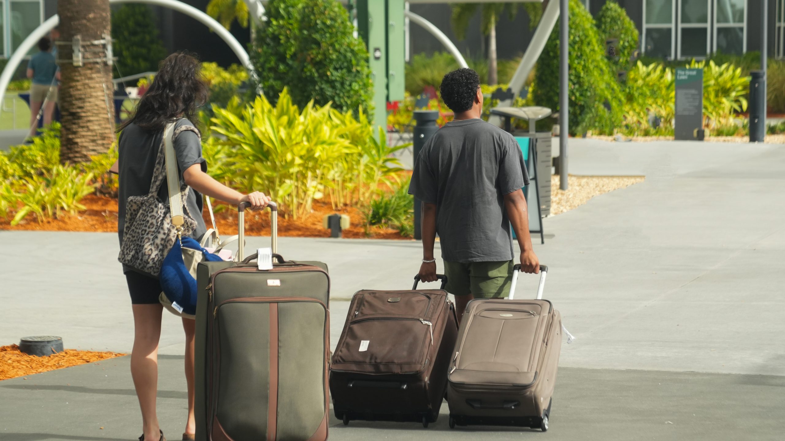Two people walking away from the camera and carrying suitcases