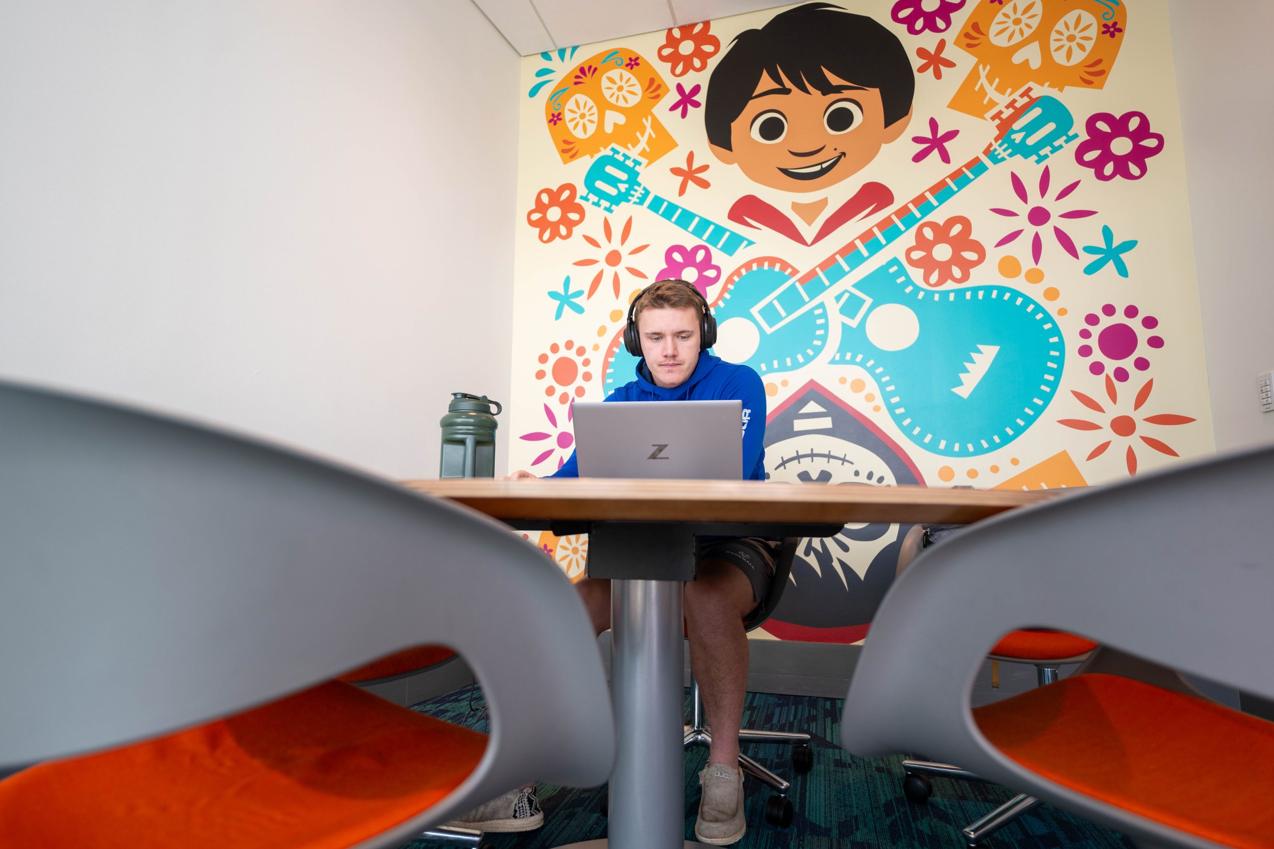 A colorful wall mural featuring Miguel from Coco provides a backdrop for a young male working at a laptop in an table in an innovation nook.