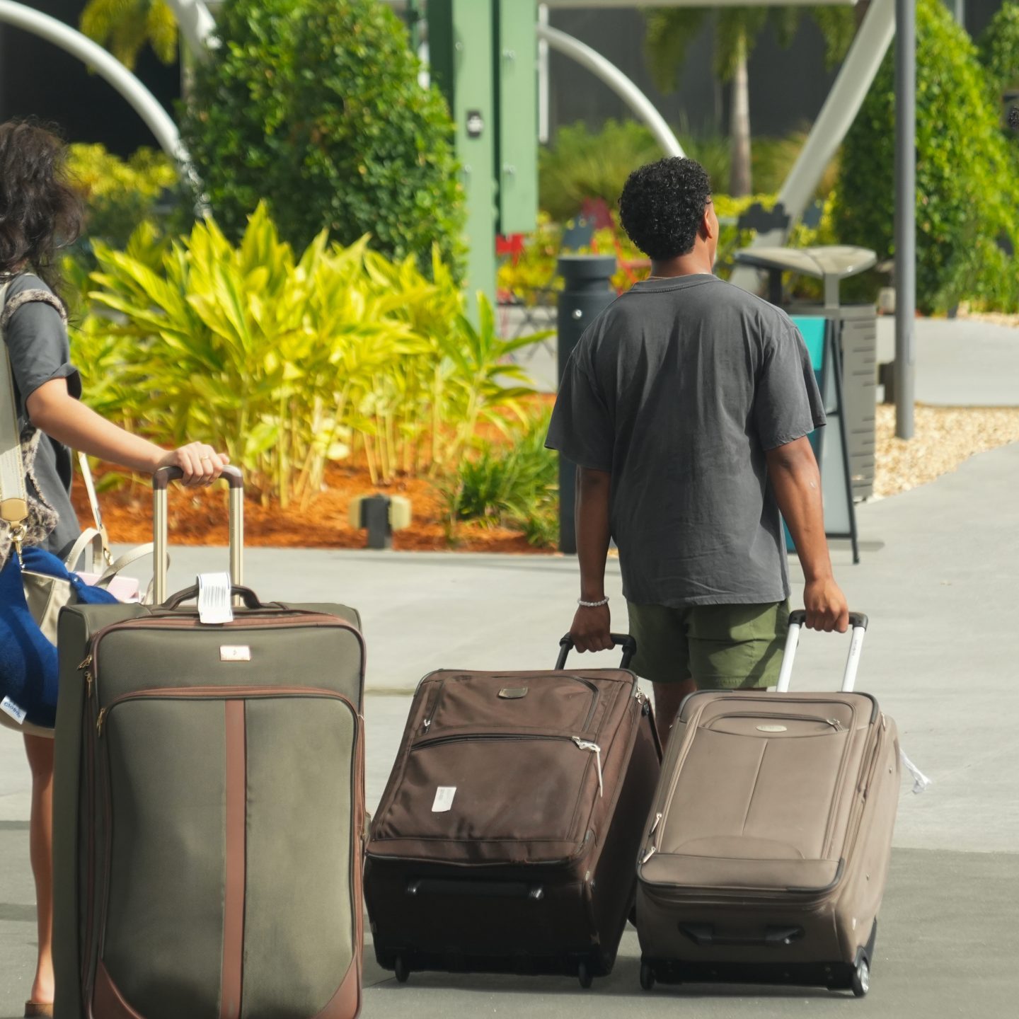 Two people walking away from the camera and carrying suitcases