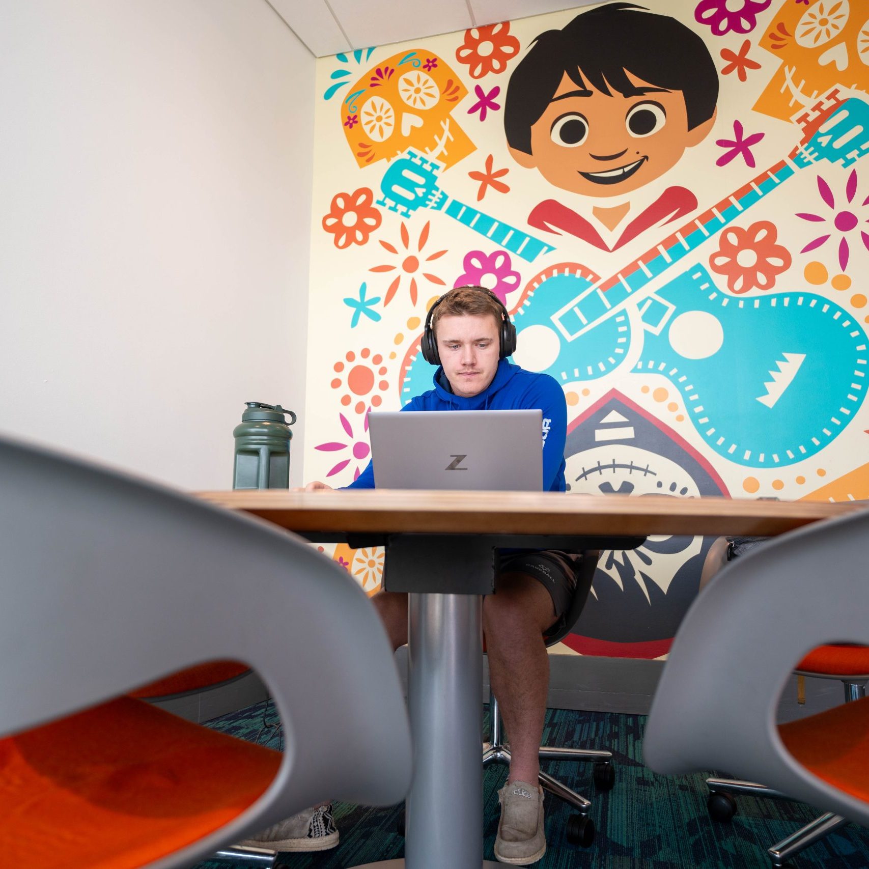 A colorful wall mural featuring Miguel from Coco provides a backdrop for a young male working at a laptop in an table in an innovation nook.