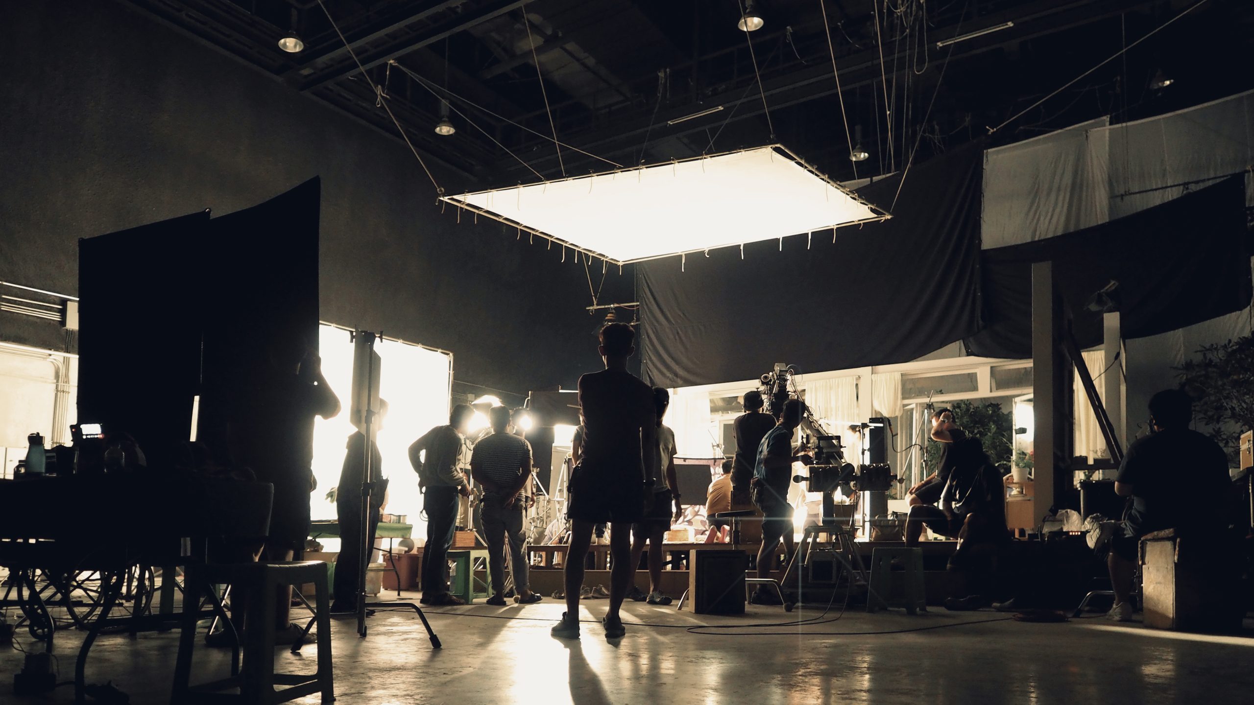 Silhouette of people working in big production studio for shooting or recording movie video by digital camera and lighting set.